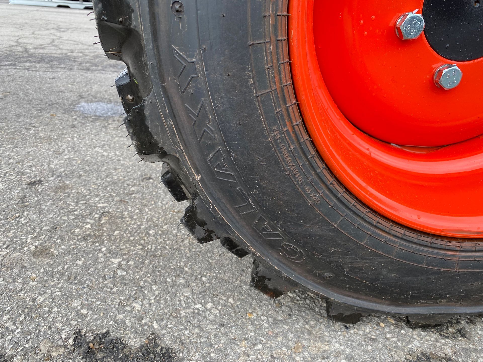 Close-up of a tractor tire and bright orange wheel on a gray surface.