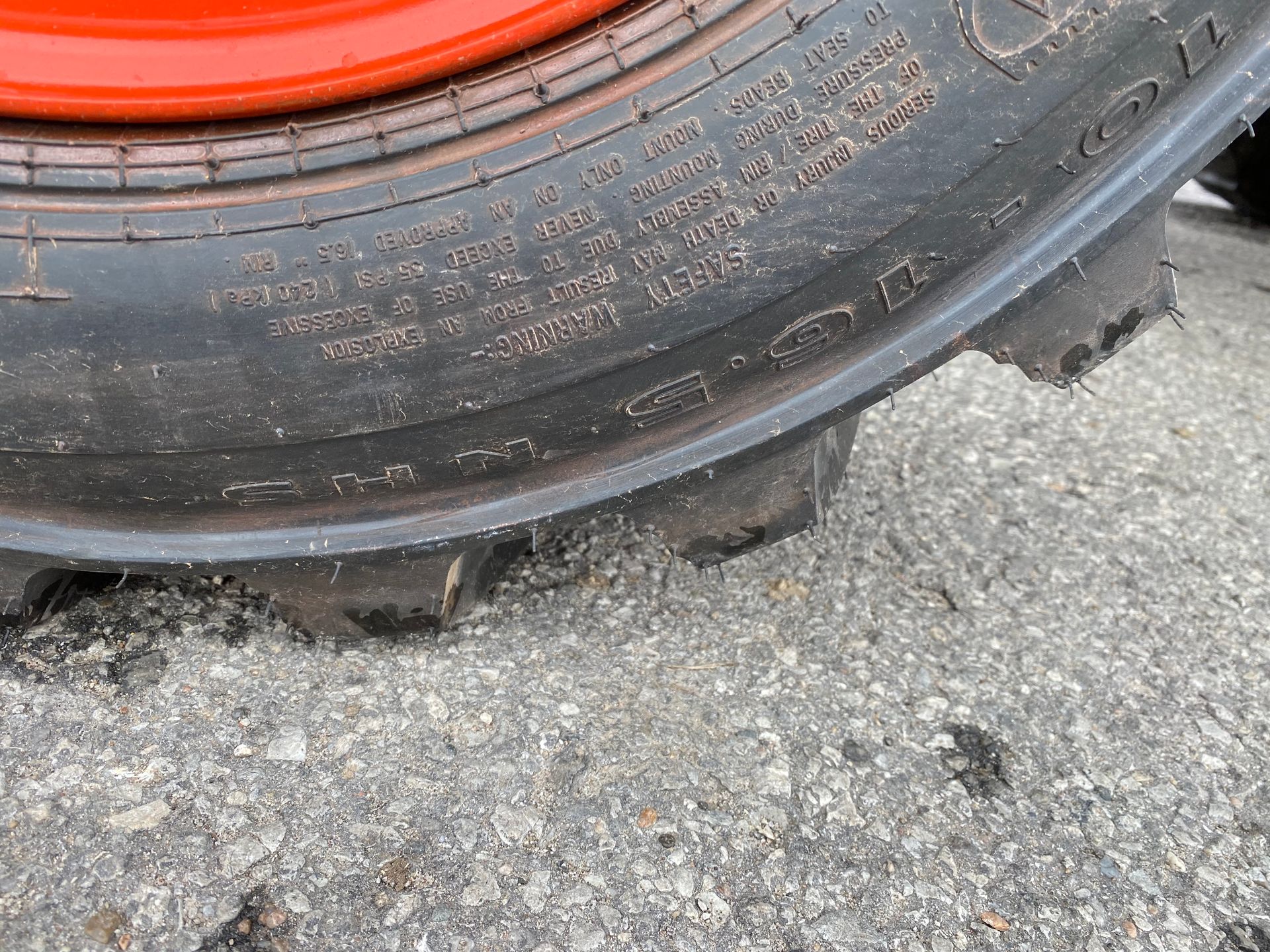 Close-up of a tractor tire with orange rim, showing tread pattern and sidewall text on a concrete surface.
