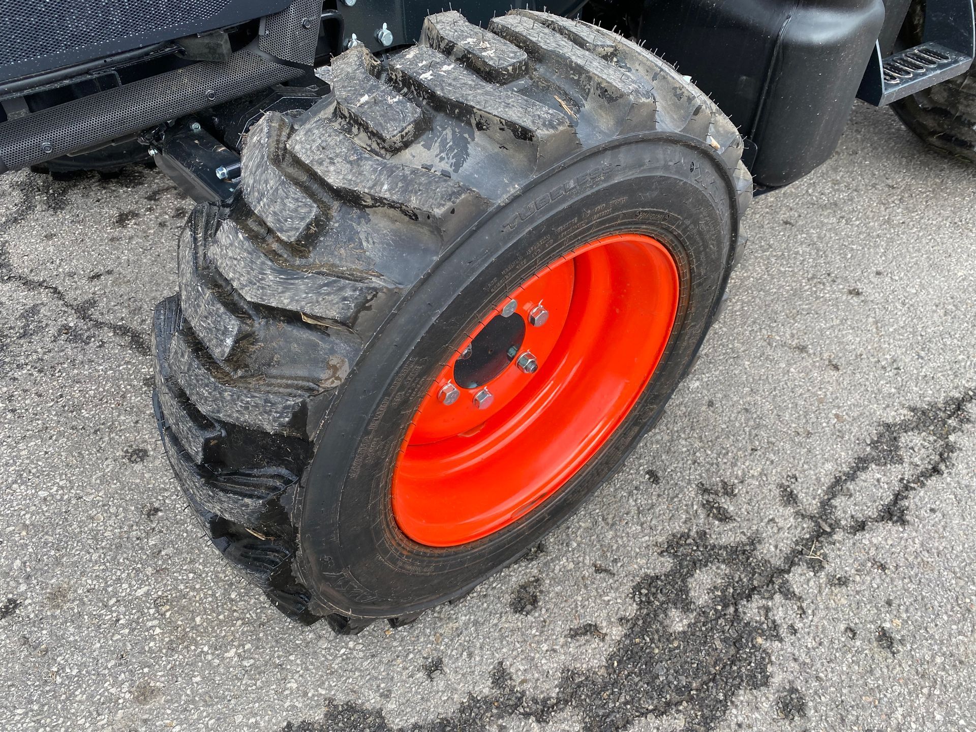 Black tractor tire on orange rim, covered in snow, resting on a gray surface.