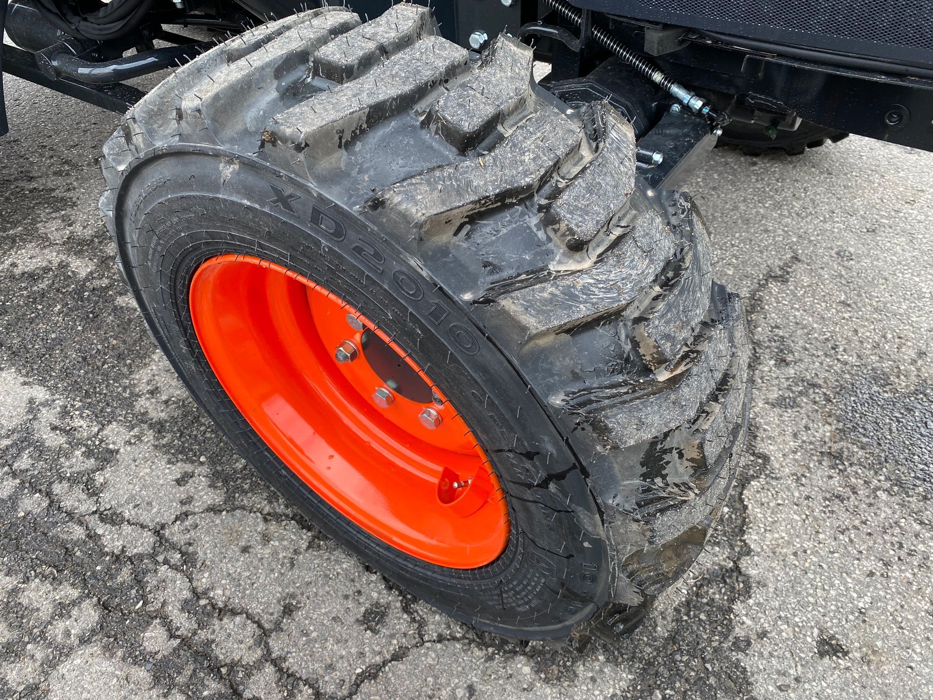 Orange rimmed tire with deep treads on a machine, sitting on gray pavement.