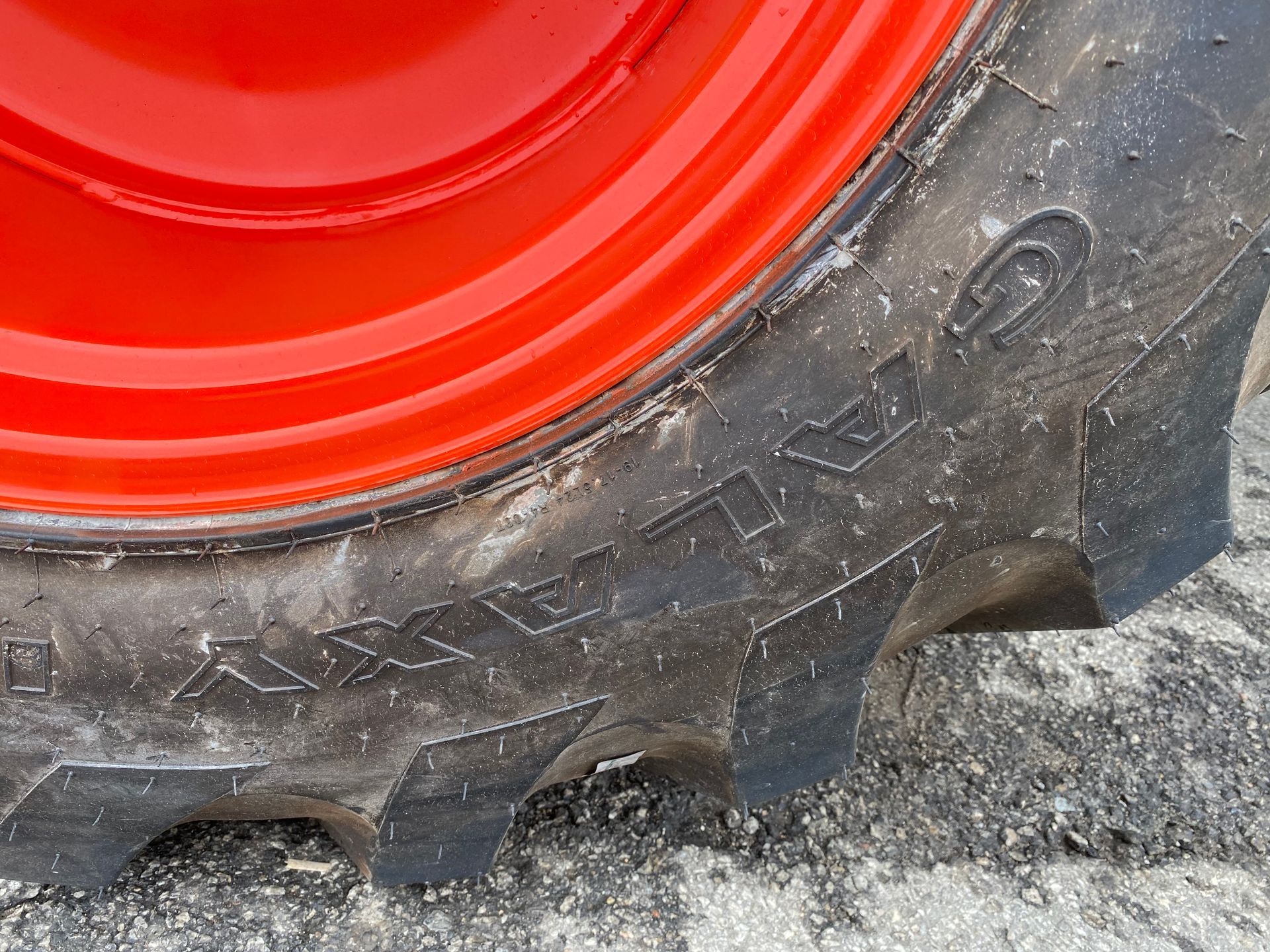Close-up of a tractor tire with black tread and a red wheel. The word 