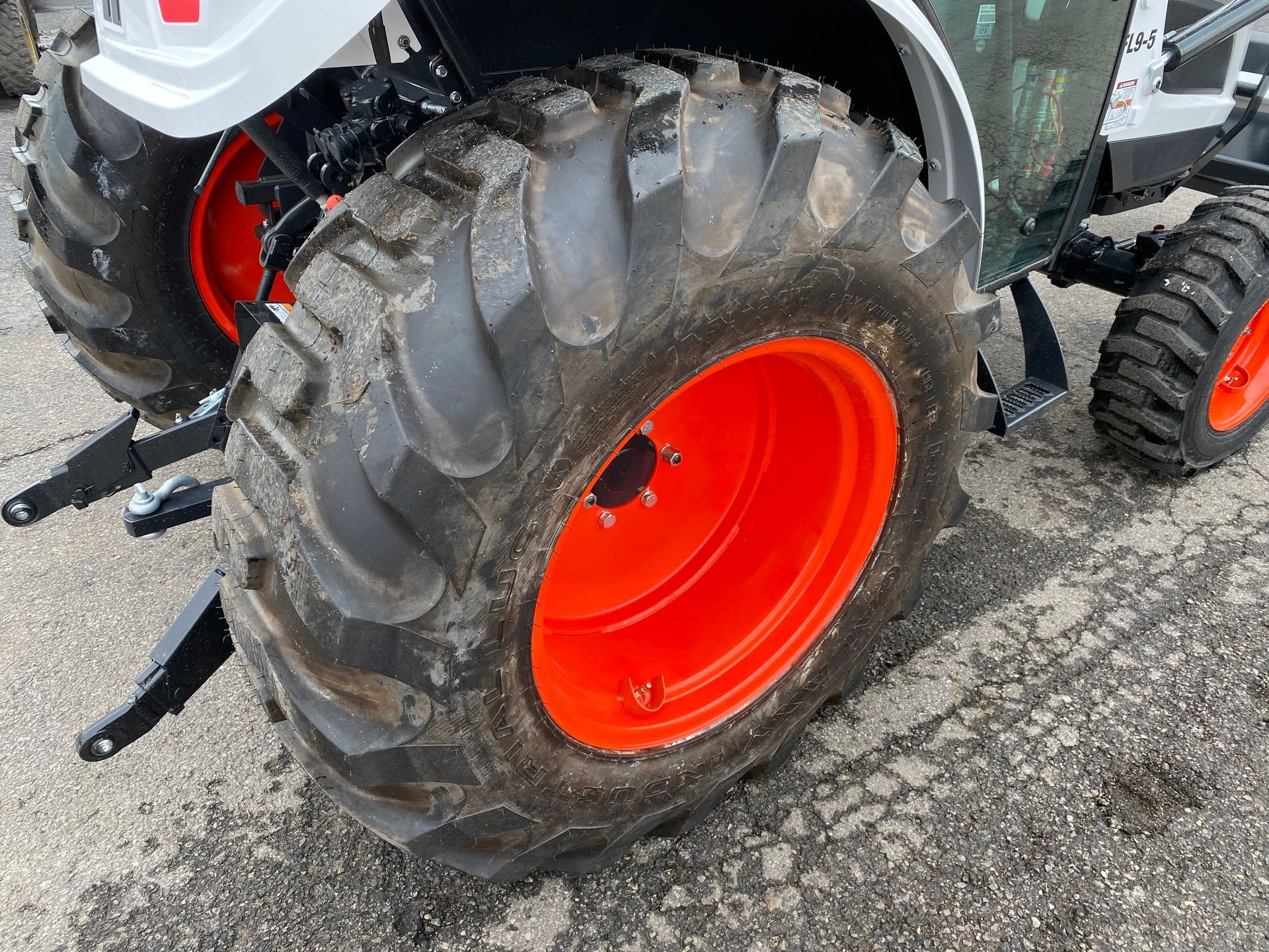 Close-up of a tractor's rear tire with a bright orange wheel. Tire is muddy with prominent tread.