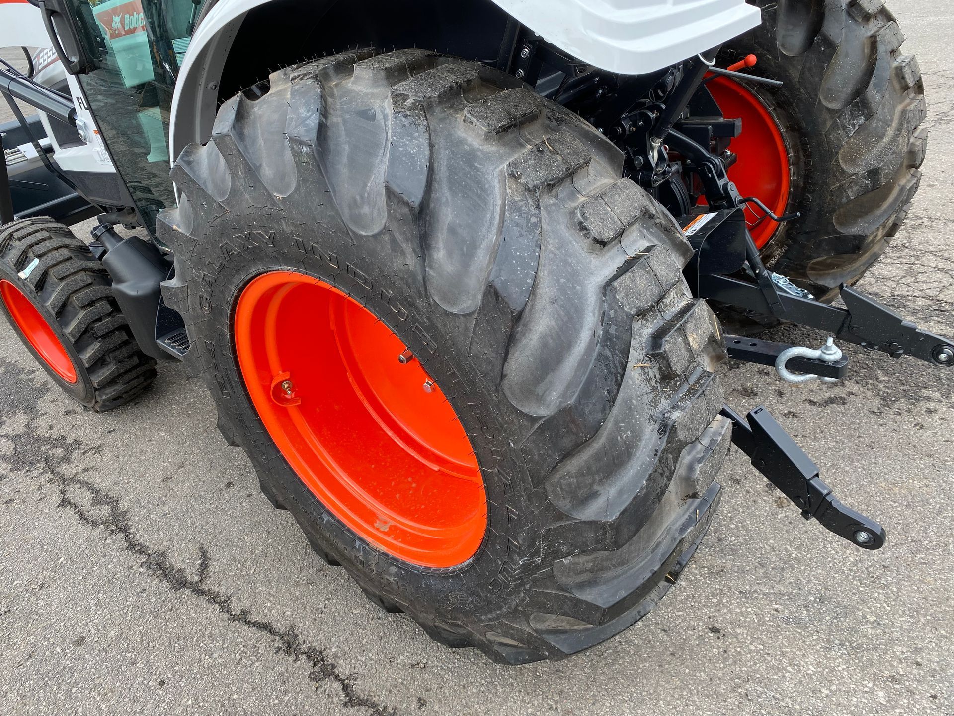 Close-up of a tractor tire with orange rim. The tractor is white and black, parked on pavement.