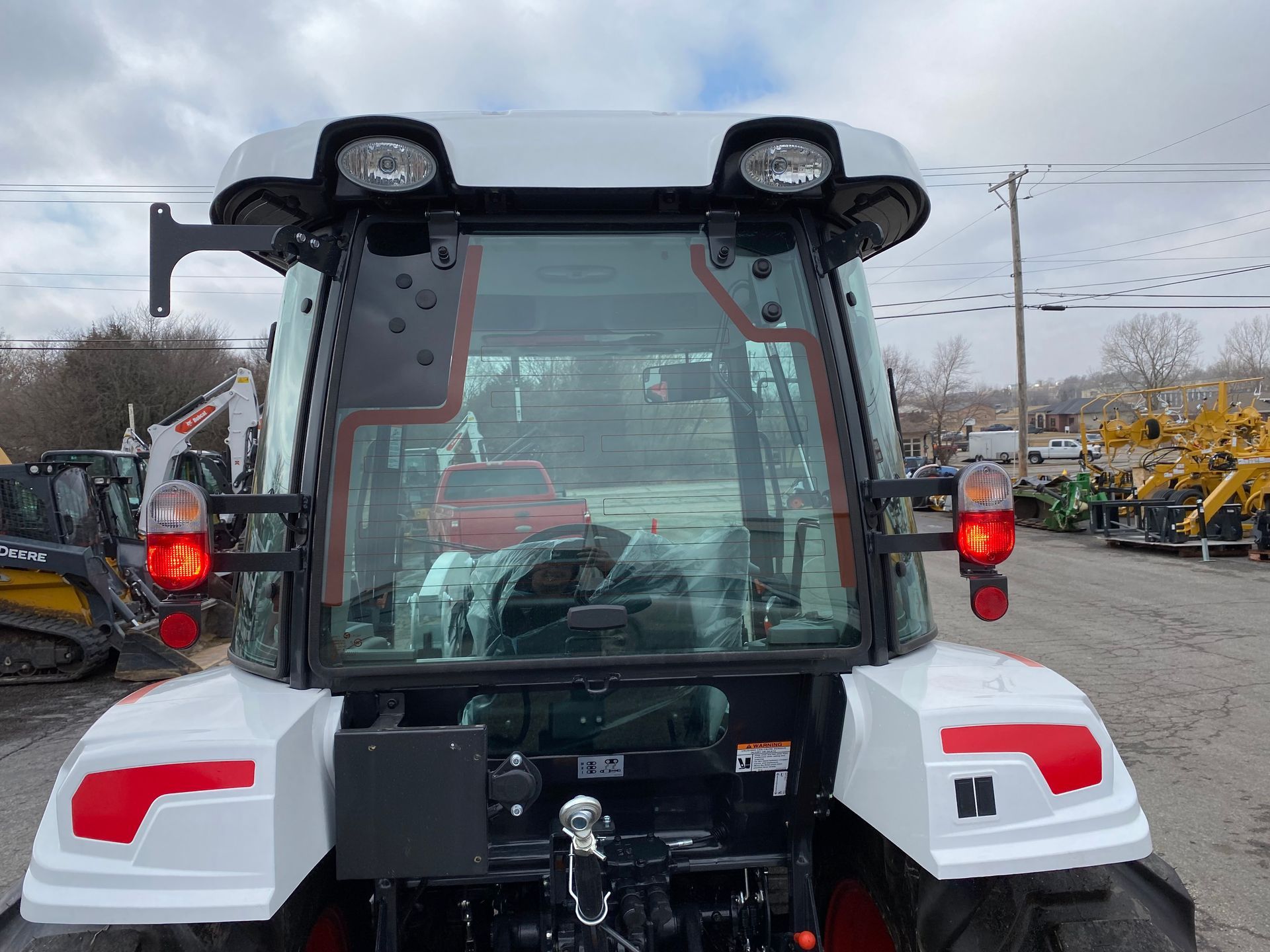 White tractor's rear view. Features include lights, glass windows, and a metal hitch, parked outside.
