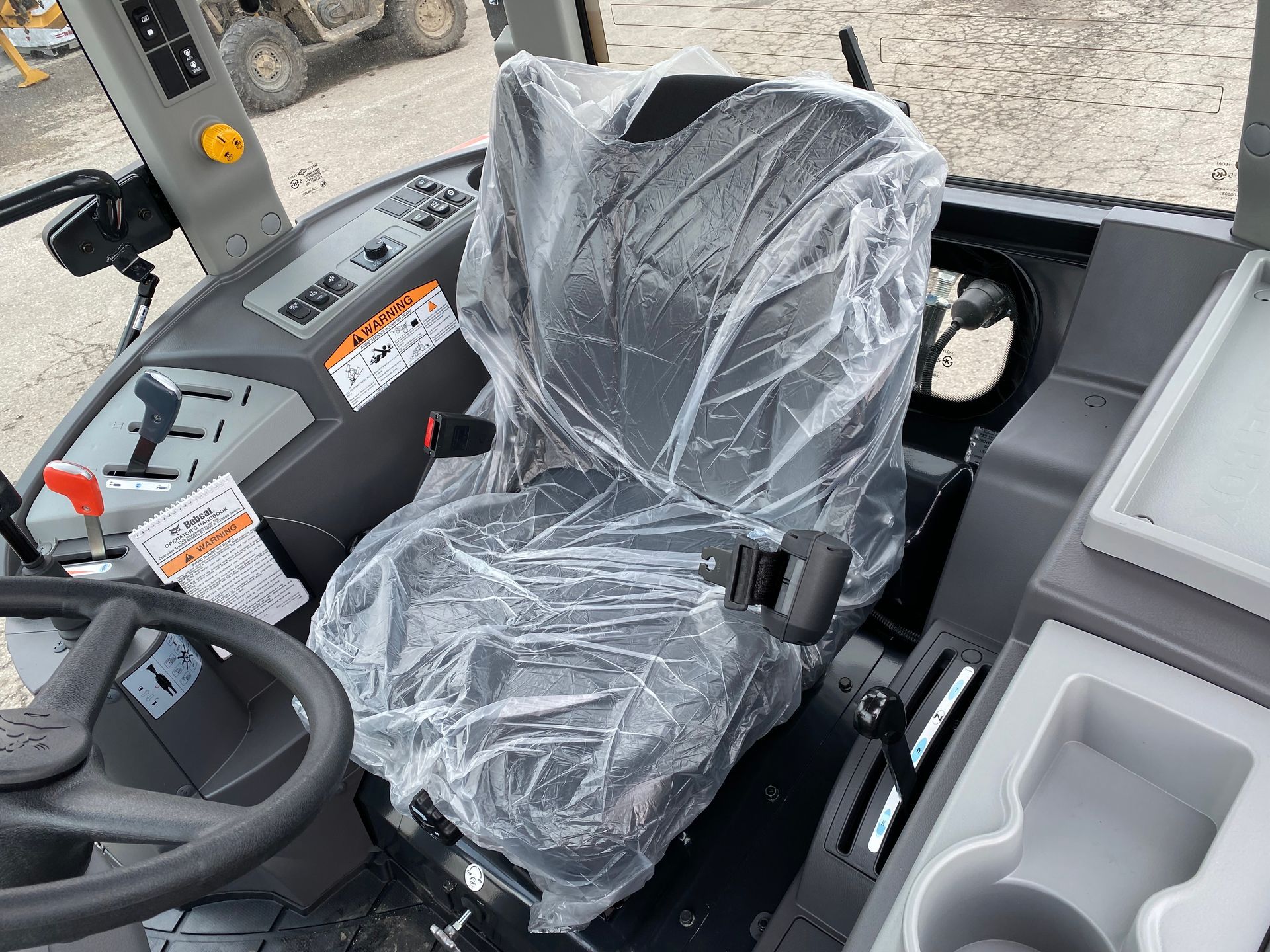 Interior of a tractor cab with plastic-covered seat, steering wheel, and control panel.