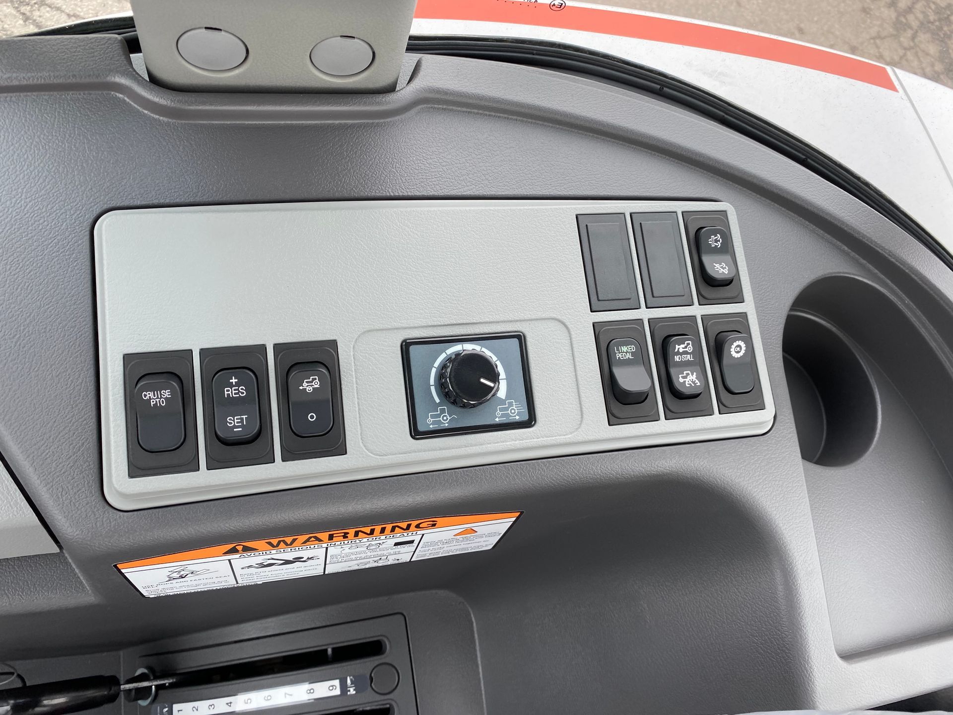 Dashboard with switches, knob, and cup holder. Grey and black color scheme, with warning label below.