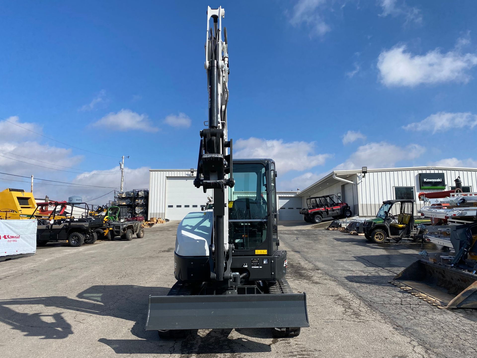Bobcat mini excavator parked outdoors on a gravel lot under a partly cloudy sky.