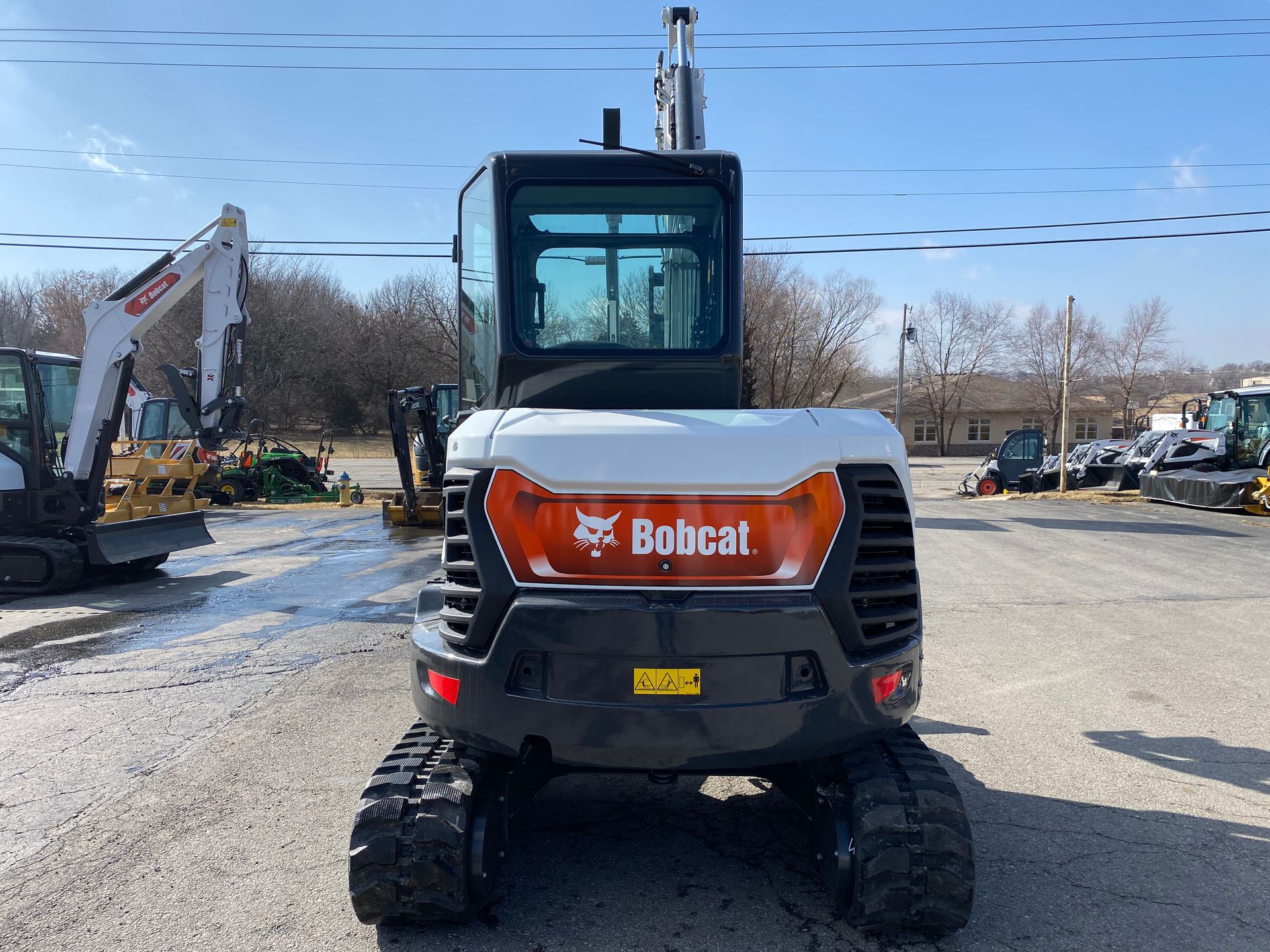 Bobcat excavator, white and black, on tracks. Orange logo on front. Outdoors, sunny day.