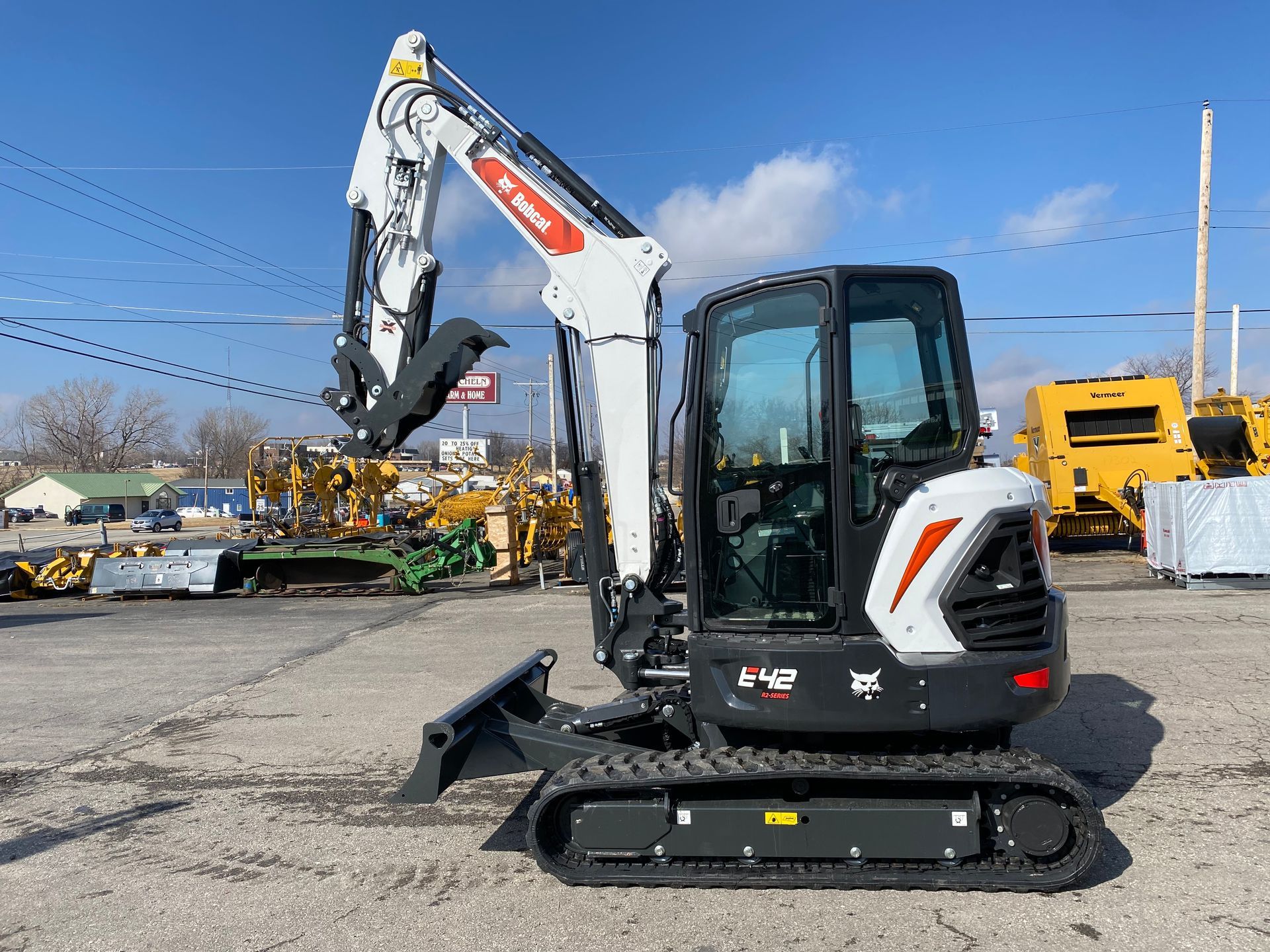 Bobcat excavator with raised arm in a lot. White and black, sunny day.