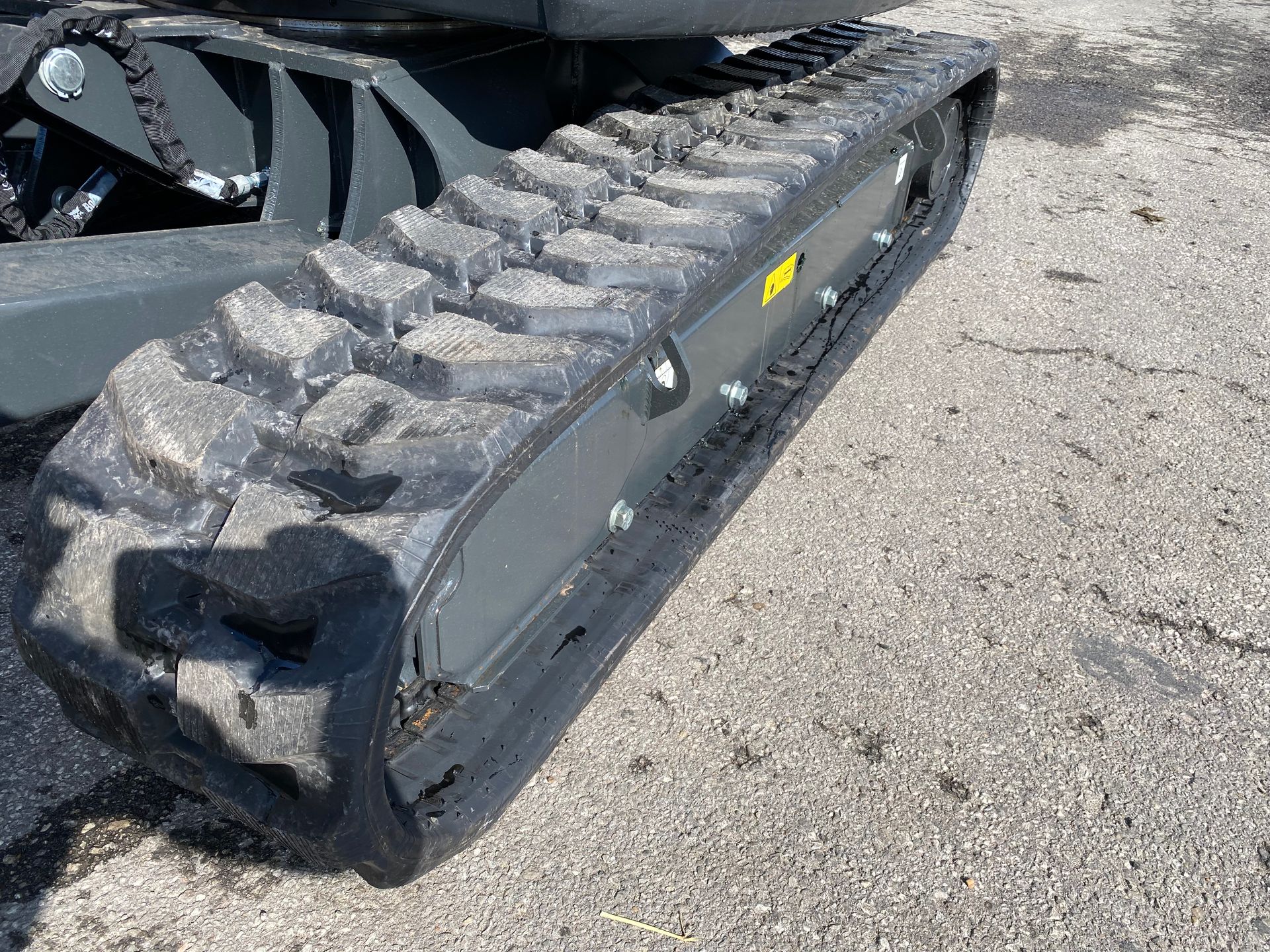 Track of a small excavator on a concrete surface. The track is dark grey with a tread pattern and appears used.