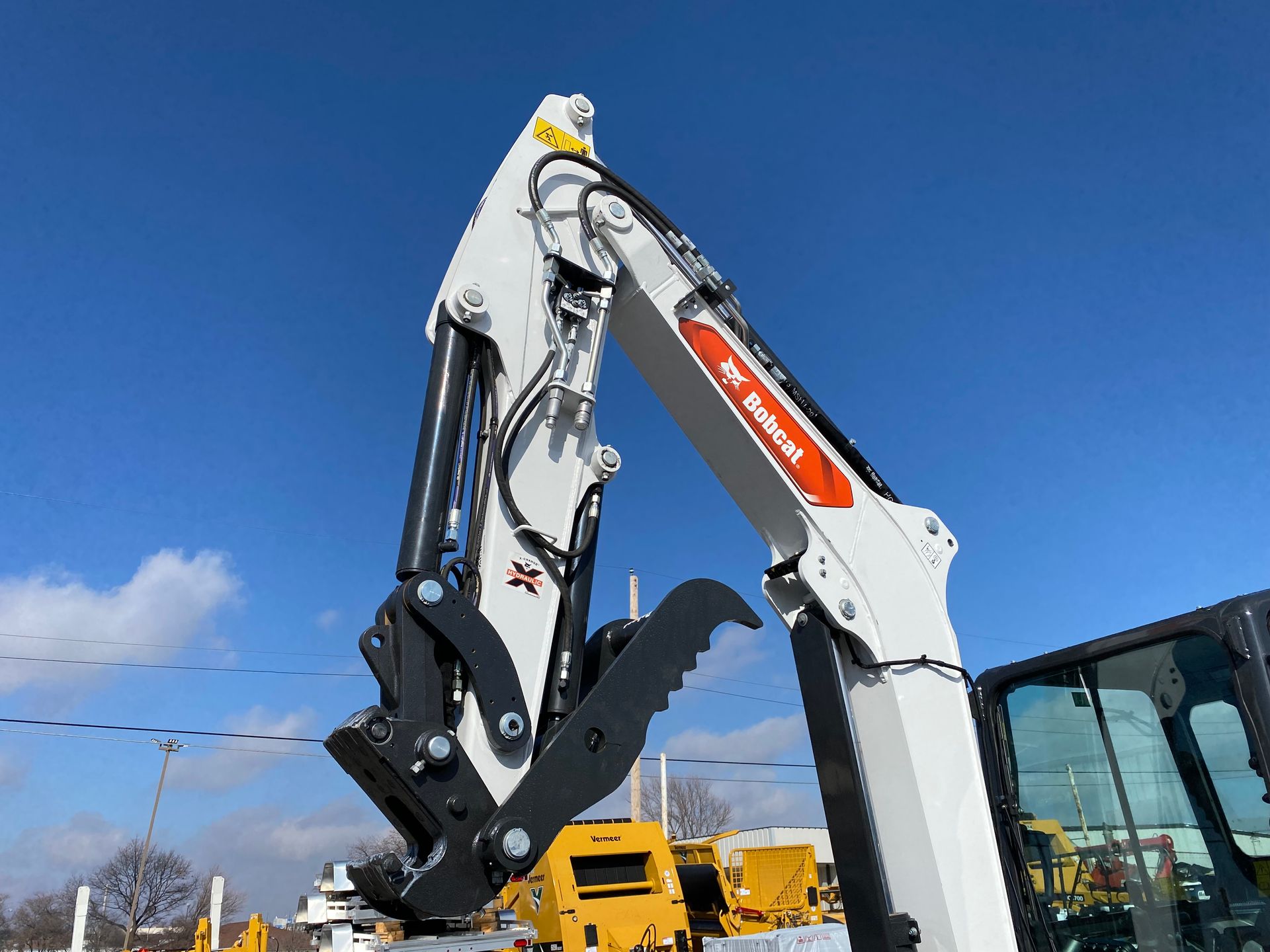 White Bobcat excavator arm with grapple against a blue sky.