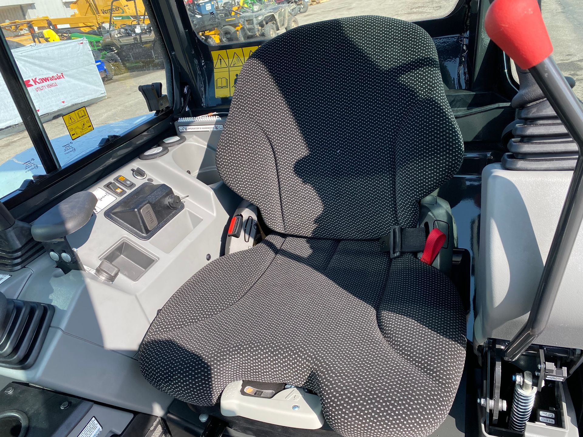 Excavator cabin interior with seat, controls, and safety belt.