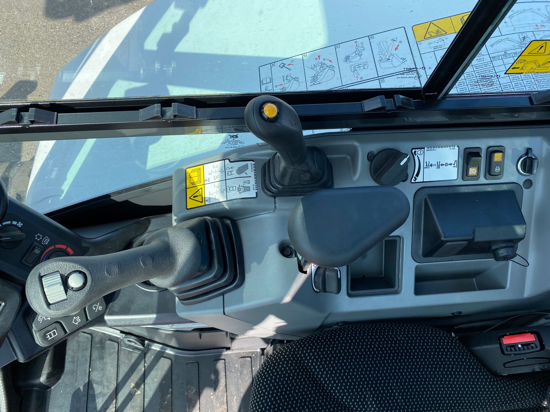 Interior of an excavator cab with joysticks, controls, and dashboard.