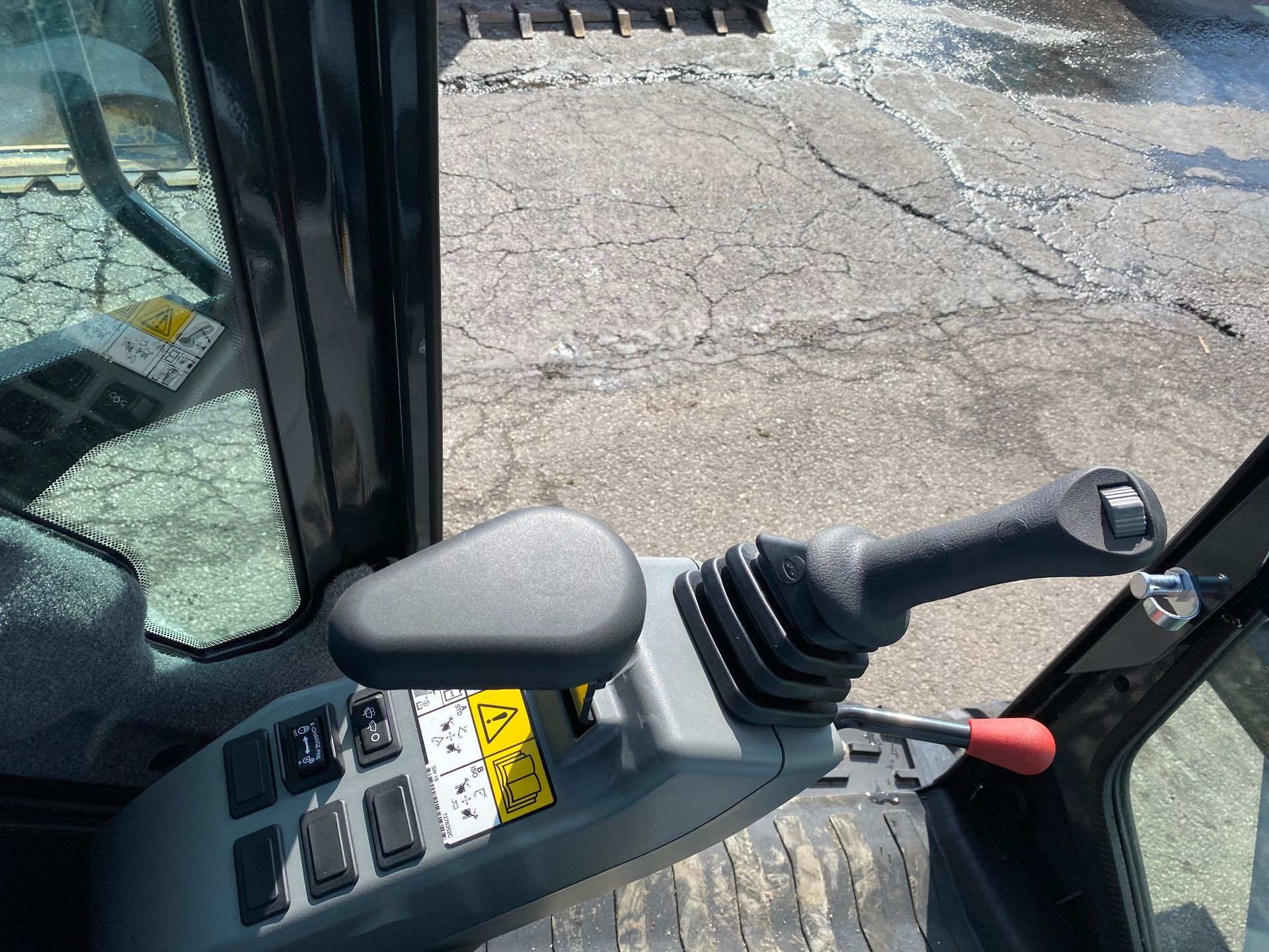 Inside cab of an excavator with control joystick, switches, and safety label.
