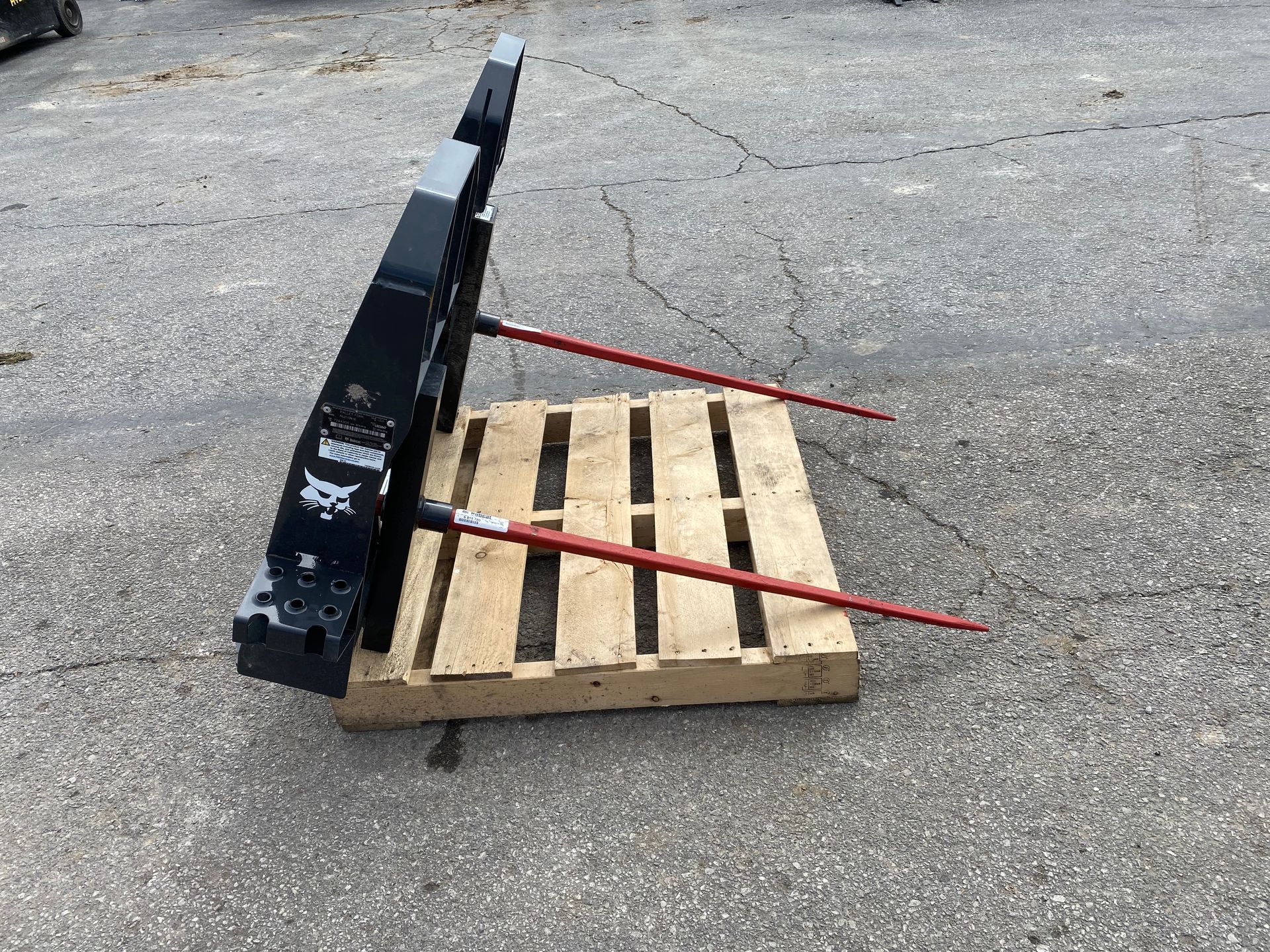 Black Bobcat bale spear attachment on a wooden pallet outdoors.