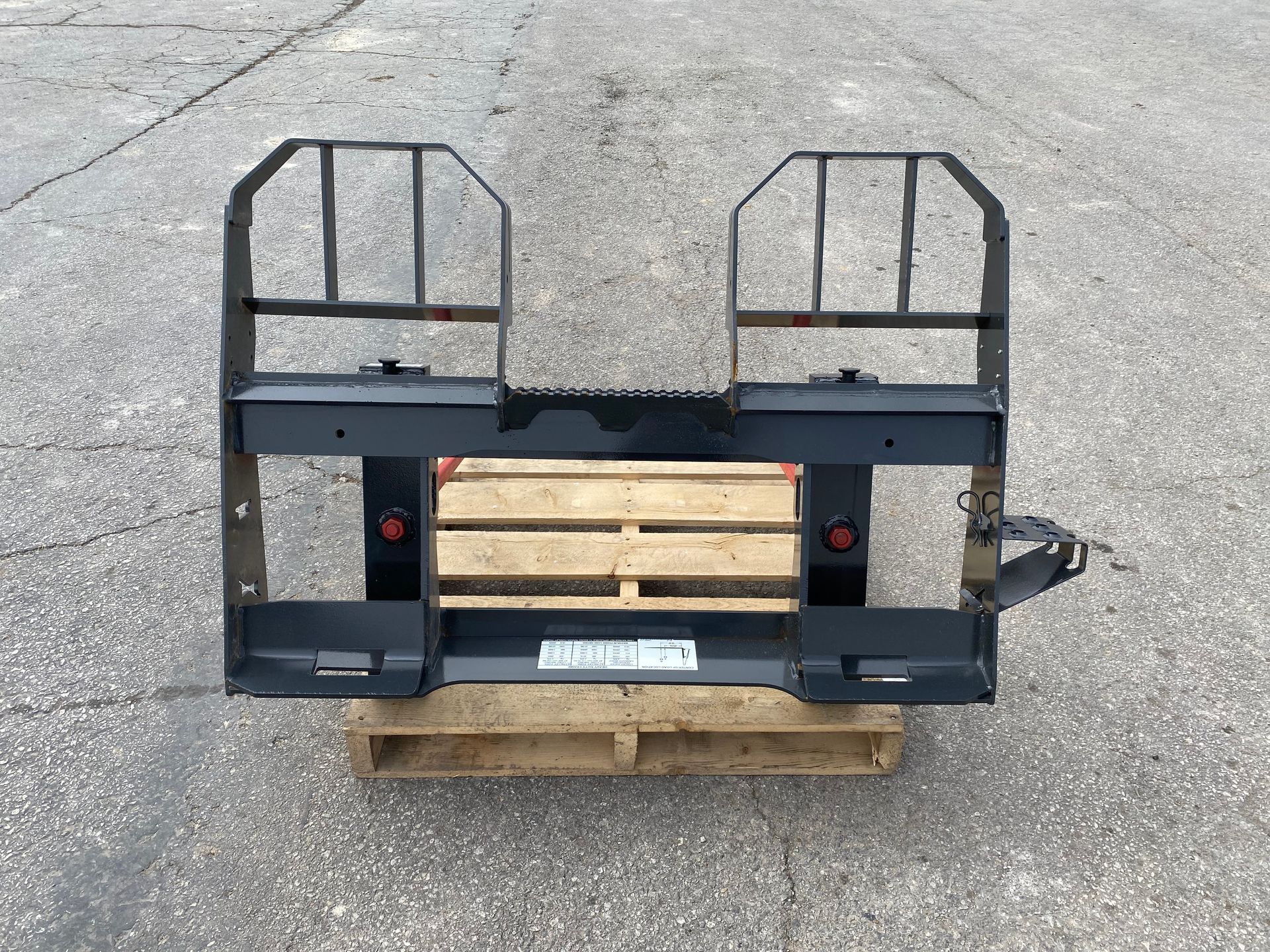 Black forklift attachment with two vertical cages, resting on a wooden pallet outdoors.