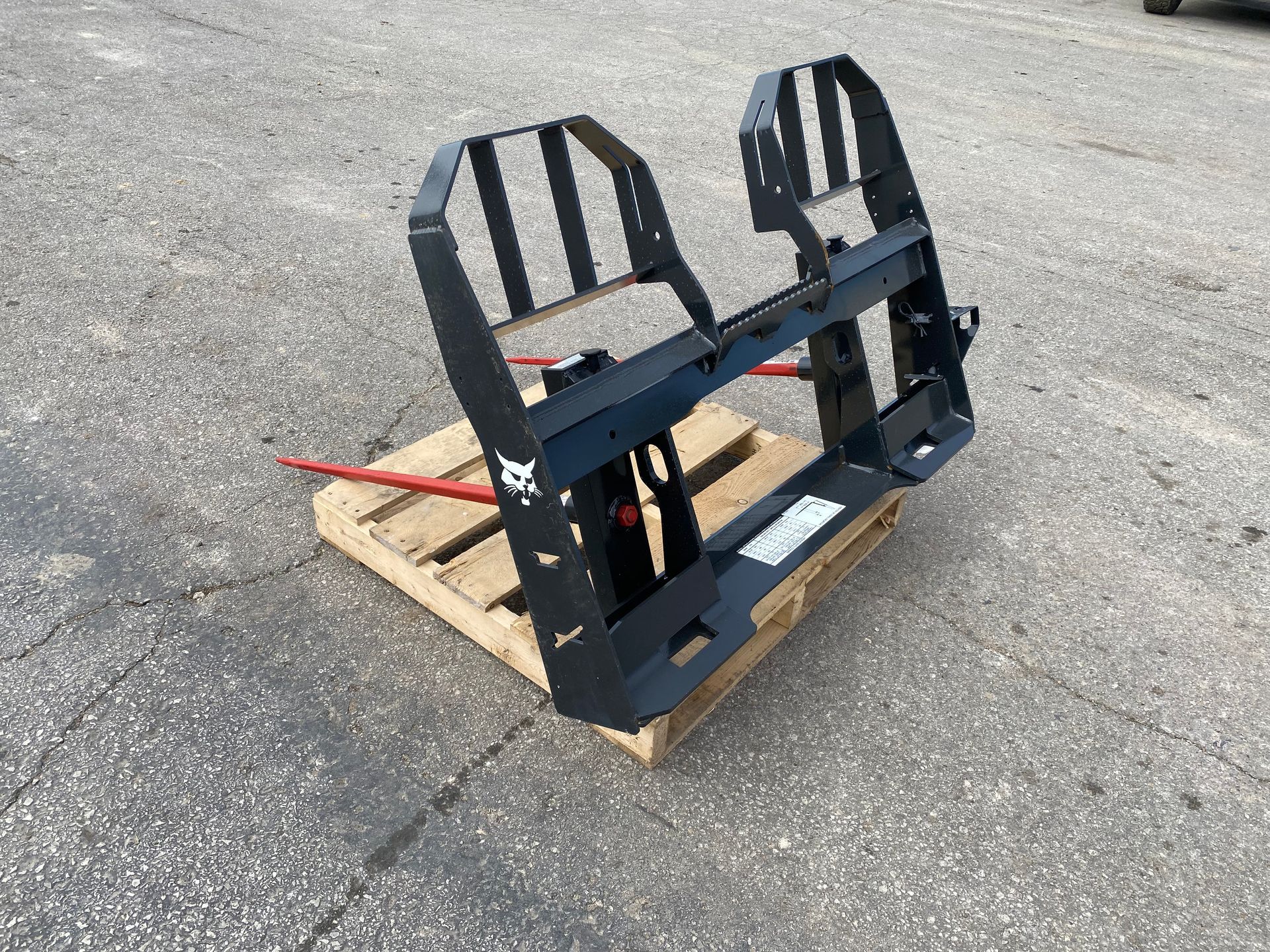 Black Bobcat bale spear attachment on a wooden pallet, outdoors.