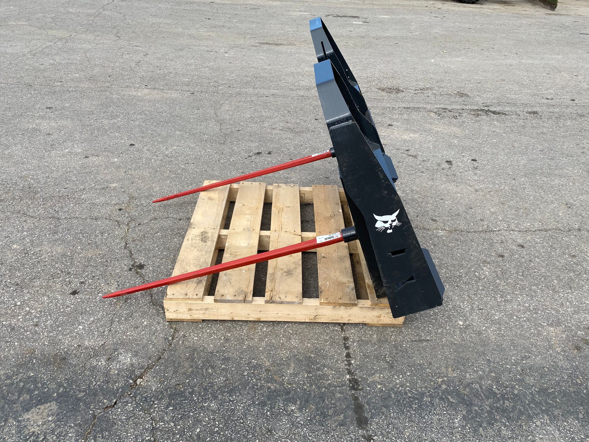 Black Bobcat hay spear attachment on a pallet outdoors. Two red tines are visible.