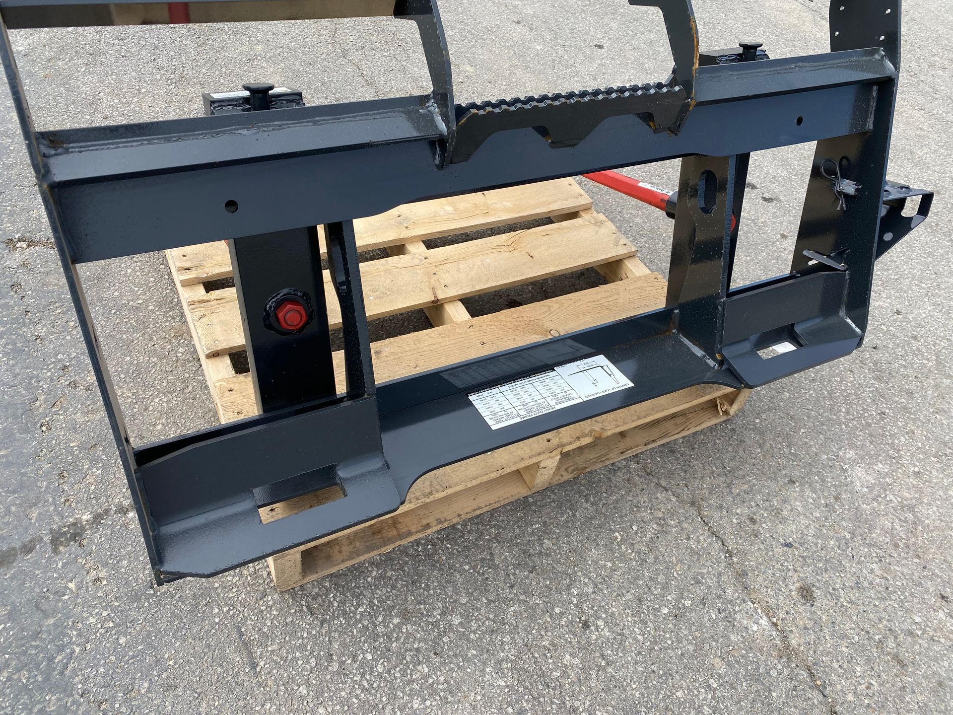 Black forklift attachment frame sits on a wooden pallet outdoors.