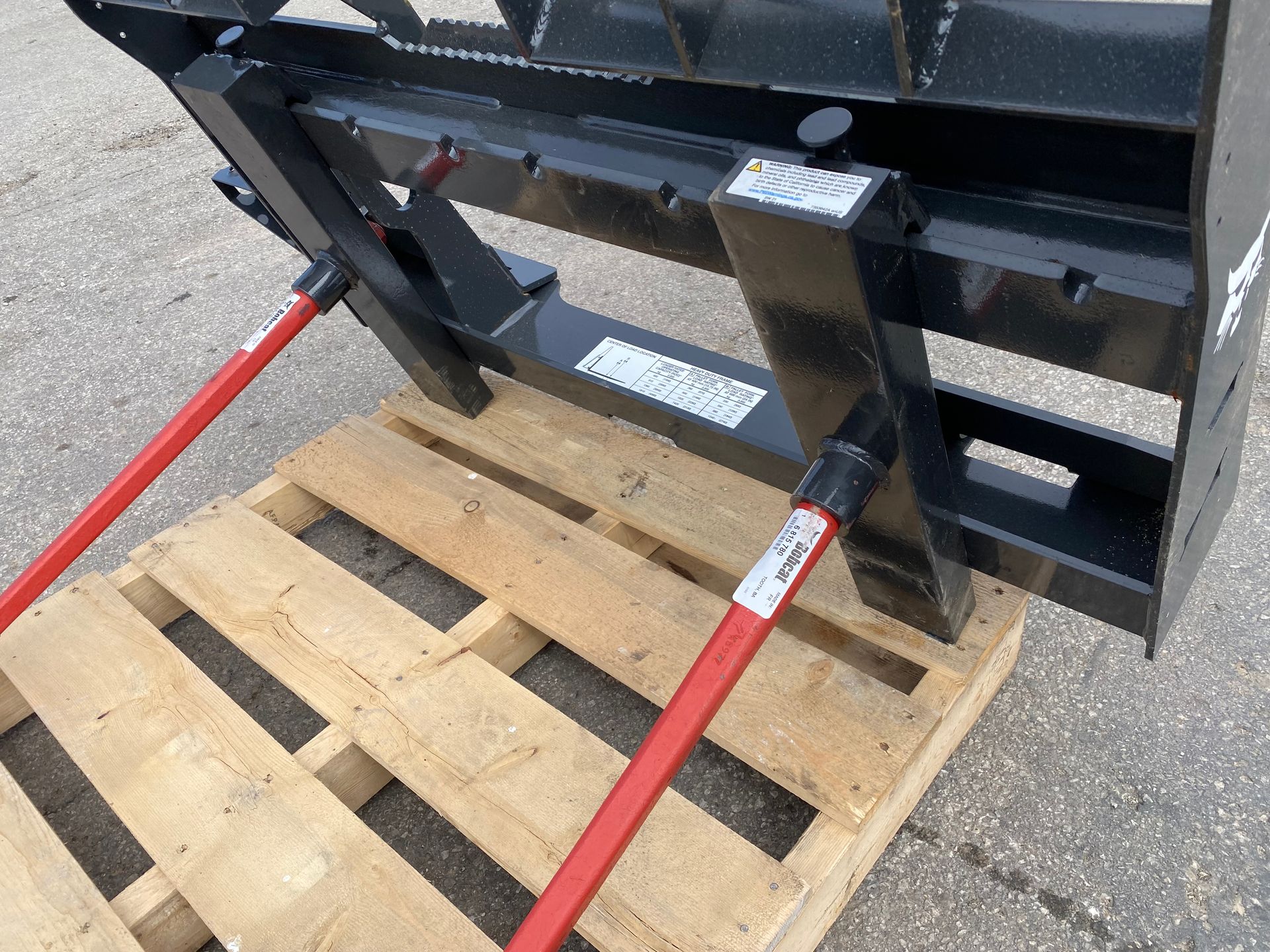 Black forklift attachment with red safety bars on a wooden pallet.