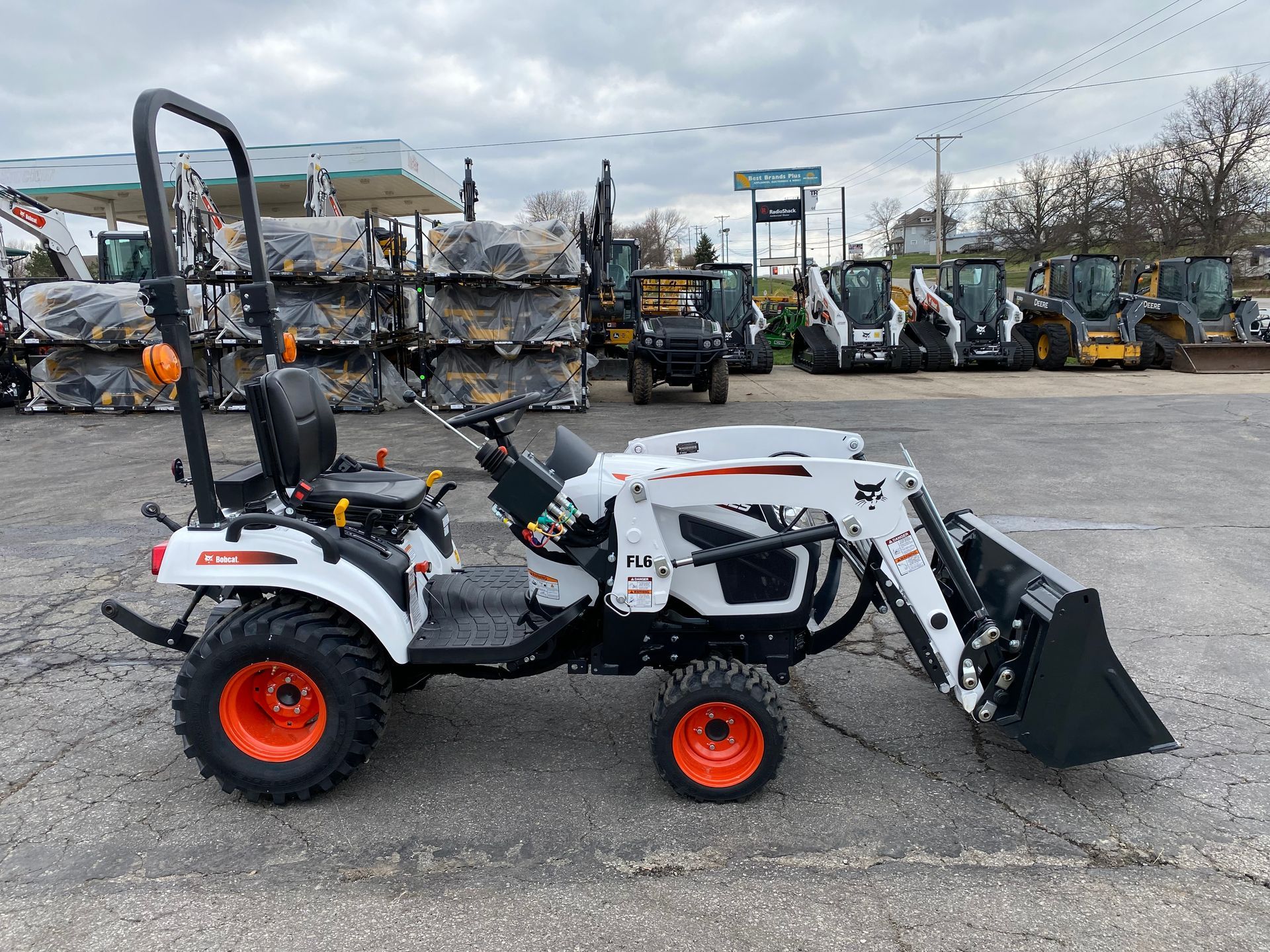 White Bobcat tractor with orange wheels and a front loader, parked outside a dealership.