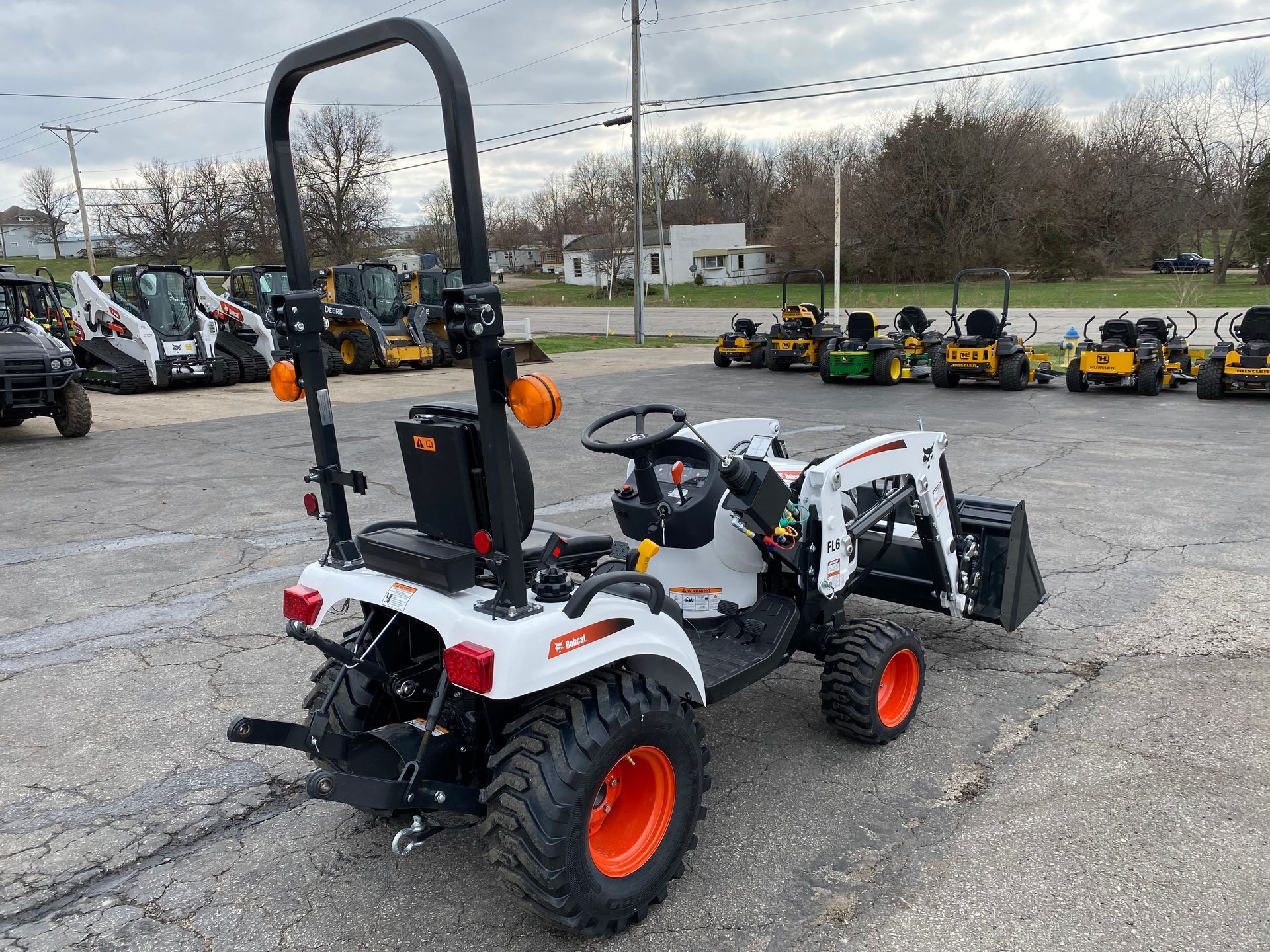 White Bobcat tractor with orange wheels and front loader parked on pavement.