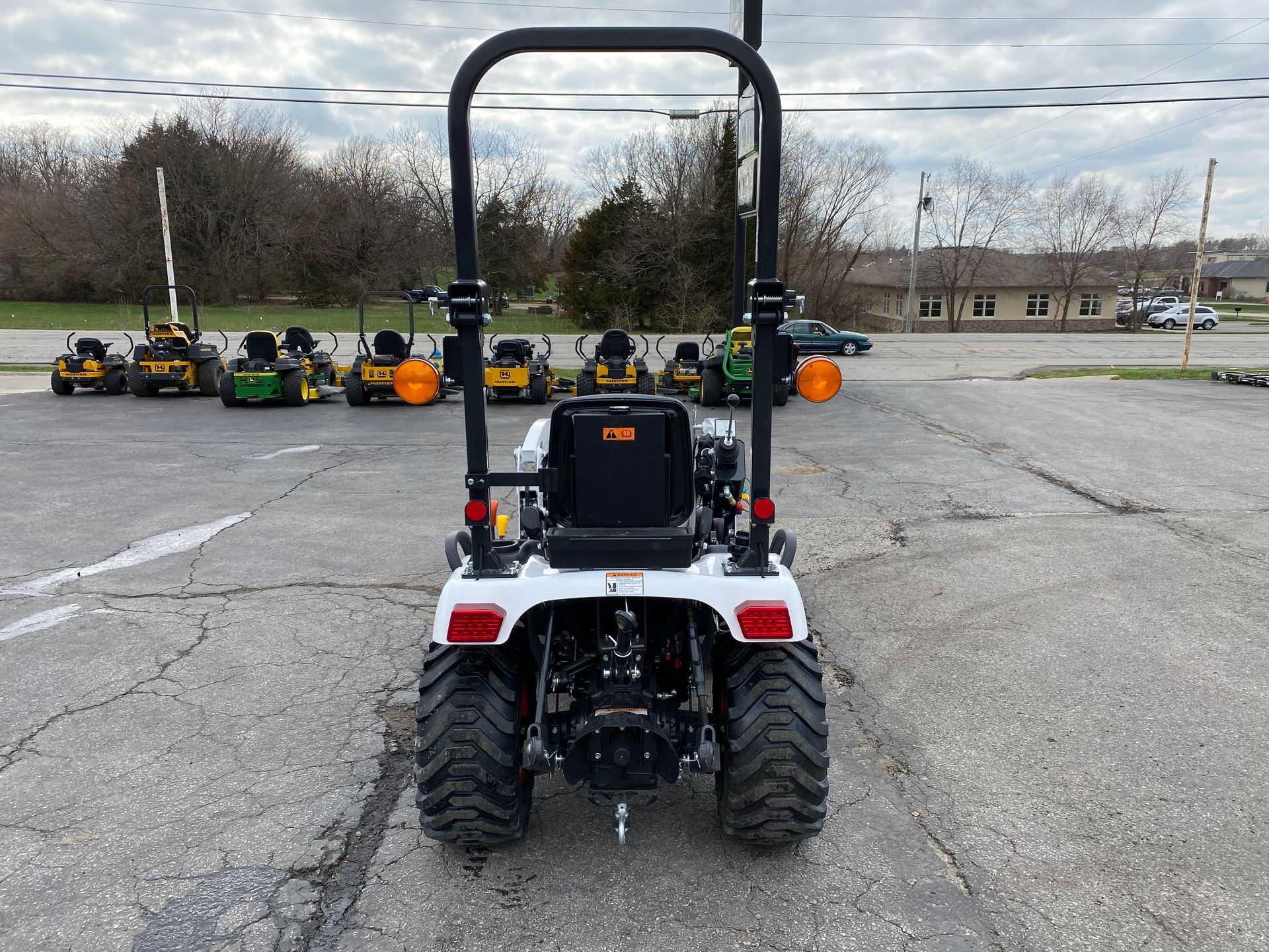 White tractor with roll bar, rear view, in parking lot. Other tractors are in background.