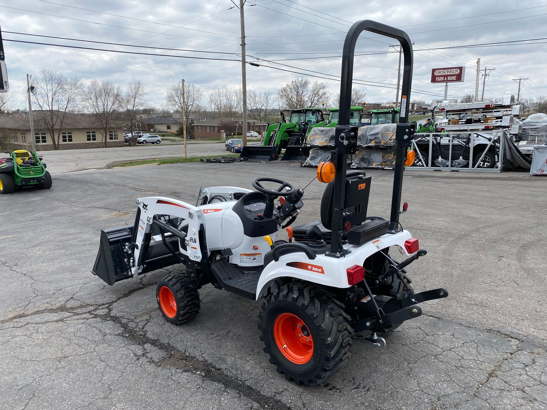 White compact tractor with orange wheels on a paved lot.