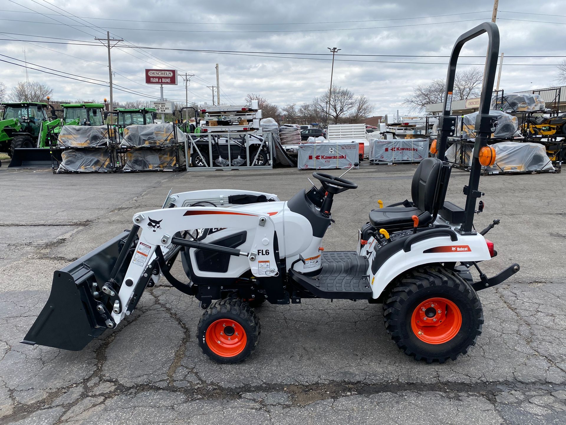 White and black Bobcat tractor with orange wheels and a front loader, parked on asphalt.