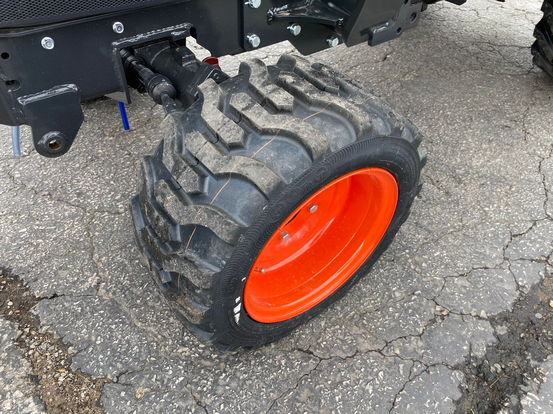 Orange-rimmed tractor tire with black tread, partially covered in dirt, on asphalt.