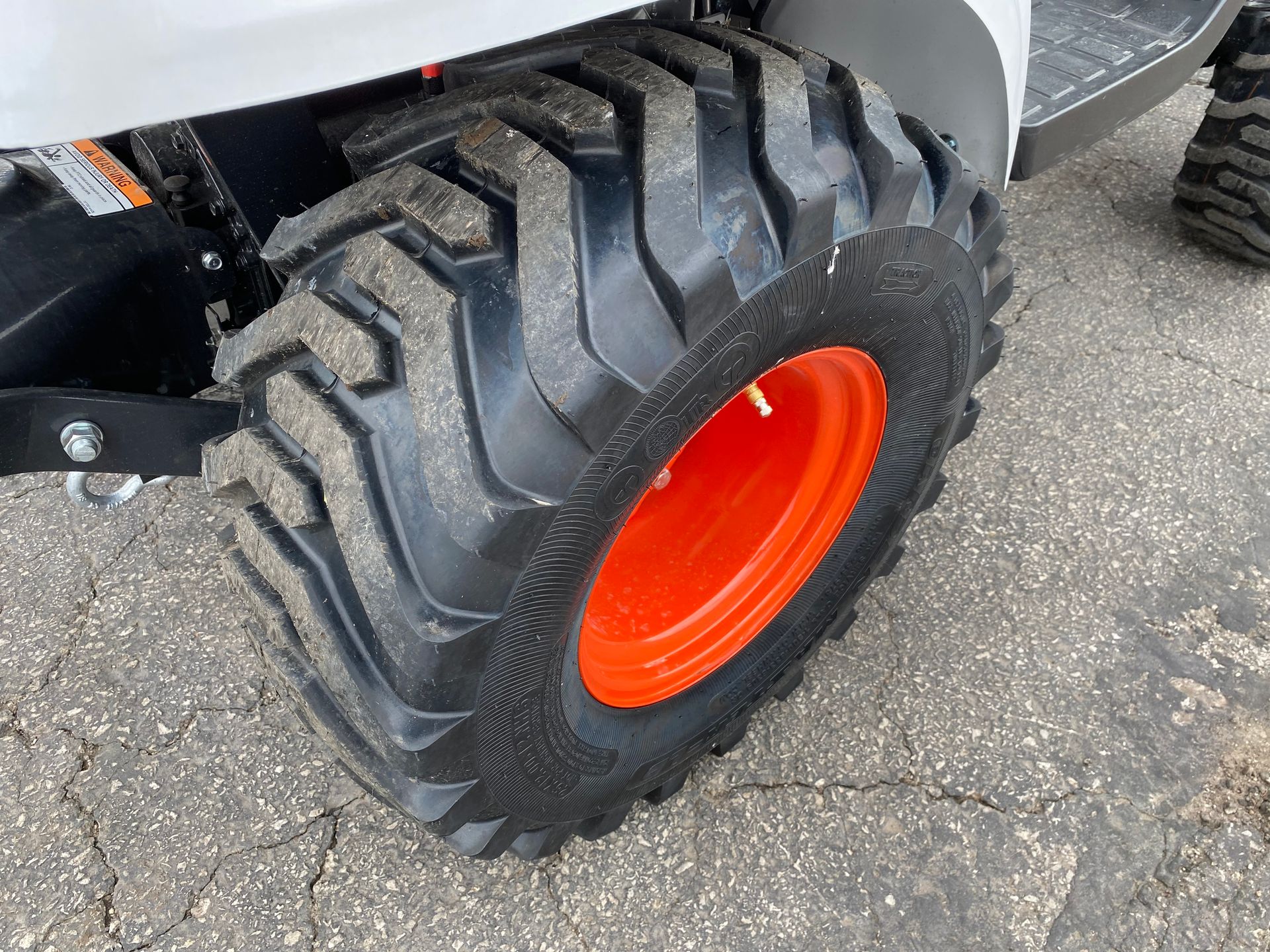 Close-up of a tractor tire with black treads and an orange wheel rim, on an asphalt surface.