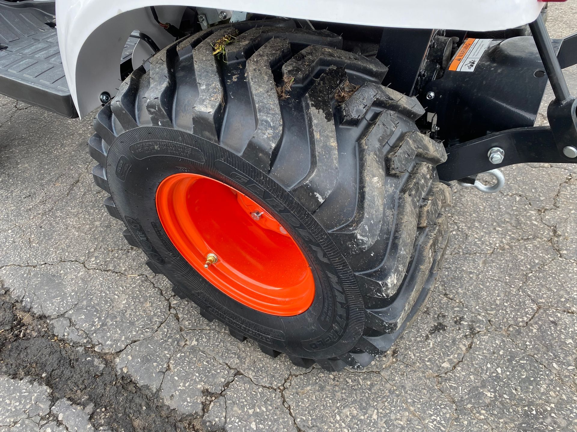 Black tractor tire with orange rim, on cracked asphalt.