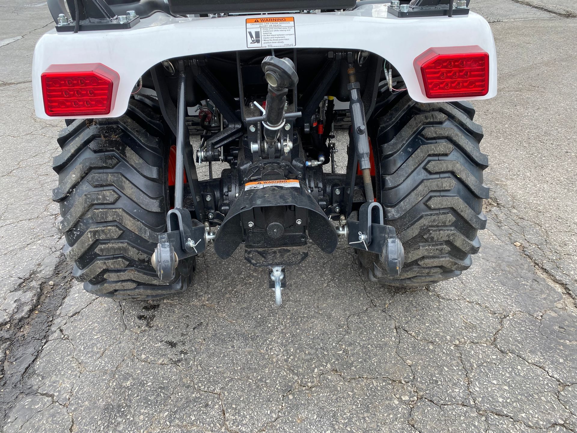 Rear view of a white tractor with large black tires on an asphalt surface.