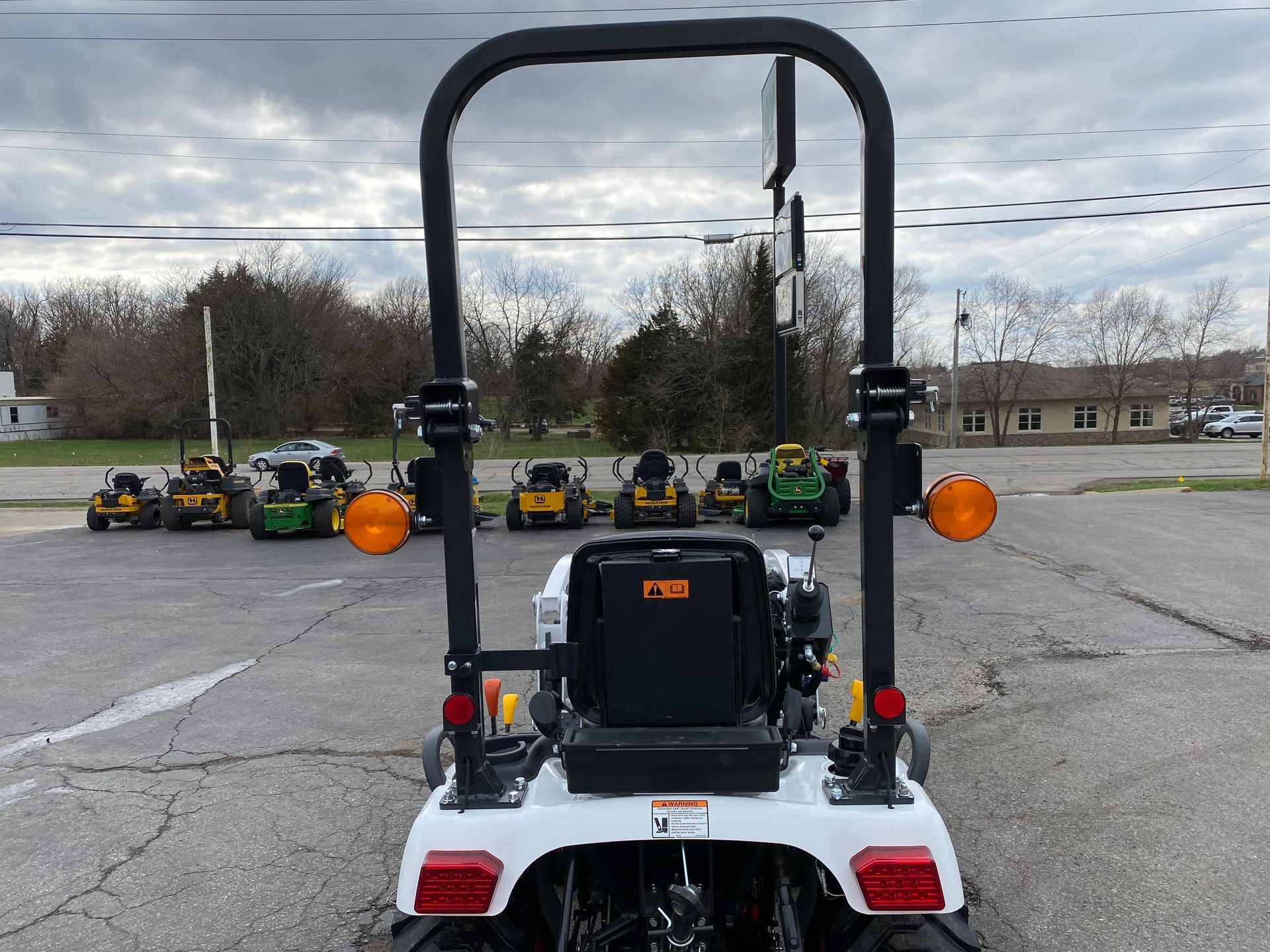White tractor with safety bar, facing away from other tractors on a cloudy day.