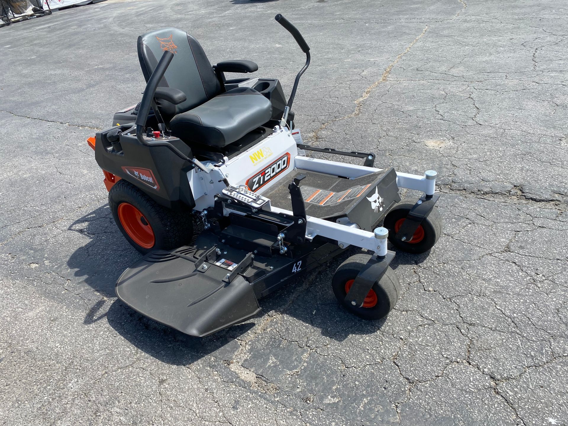 A gray Bobcat zero-turn lawnmower with a black seat and orange wheels on an asphalt surface.