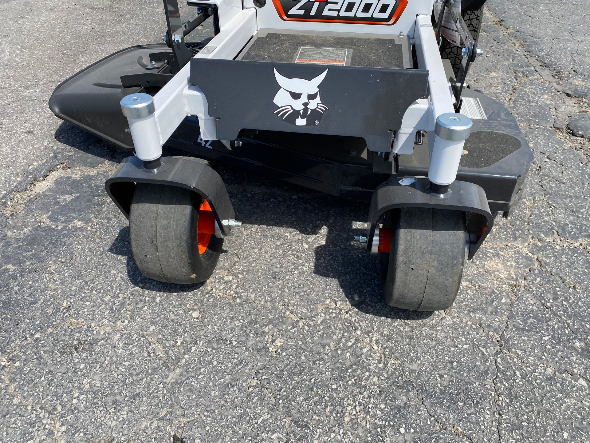 Bobcat ZT2000 zero-turn mower front view with black tires, orange accents, and a grey platform on pavement.