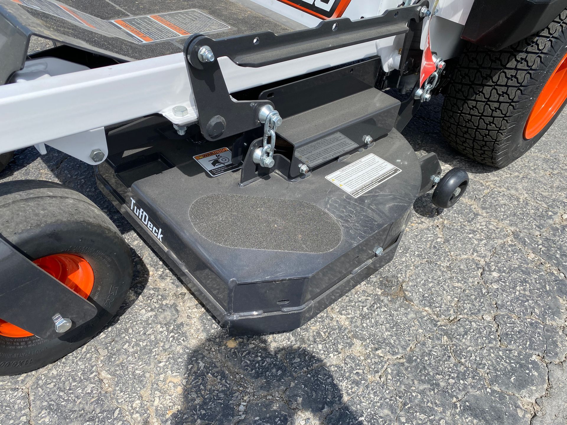 Black and orange lawn mower deck, with a Bobcat logo, on asphalt.