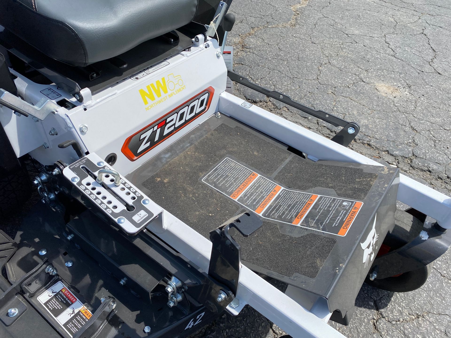 White and black zero-turn mower, controls visible, with warning labels on the footrest.