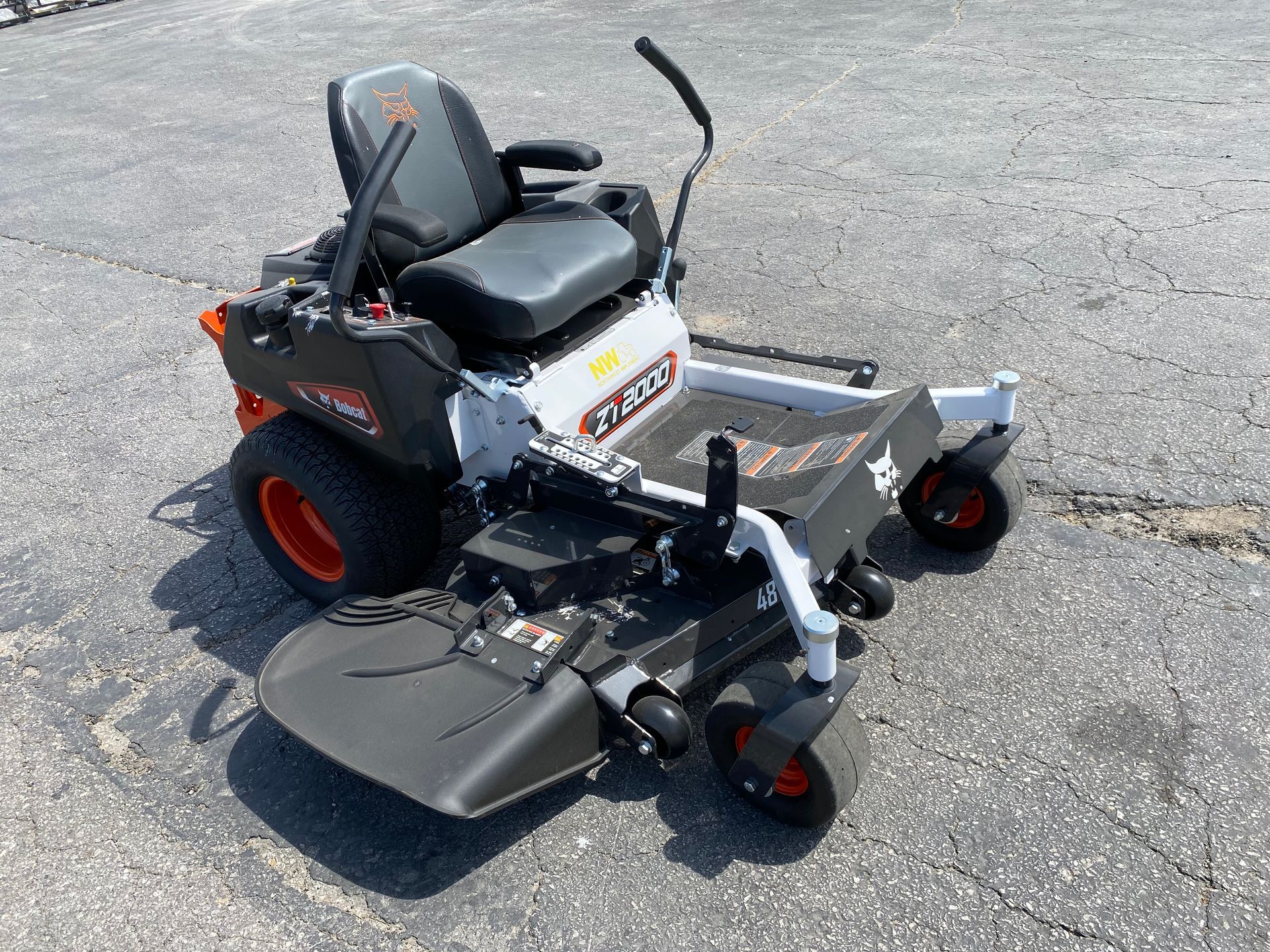 Zero-turn lawn mower with black seat and orange wheels, on pavement.
