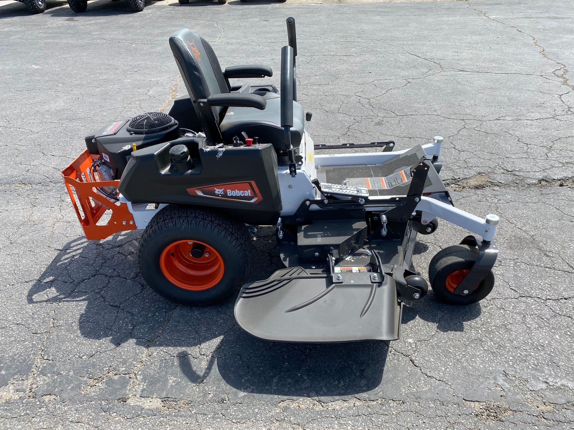 A white and orange zero-turn lawnmower on a cracked asphalt surface.