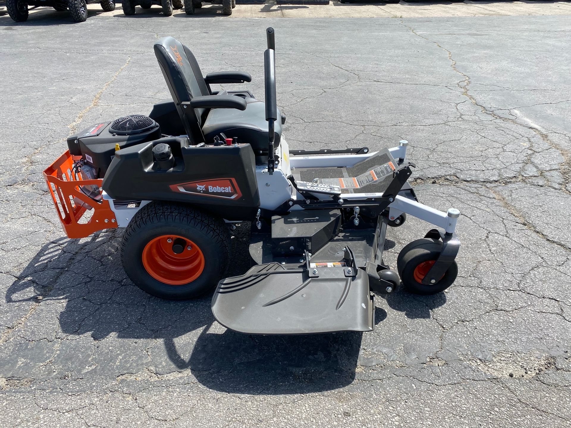 Bobcat zero-turn mower with orange wheels and basket, parked on asphalt.