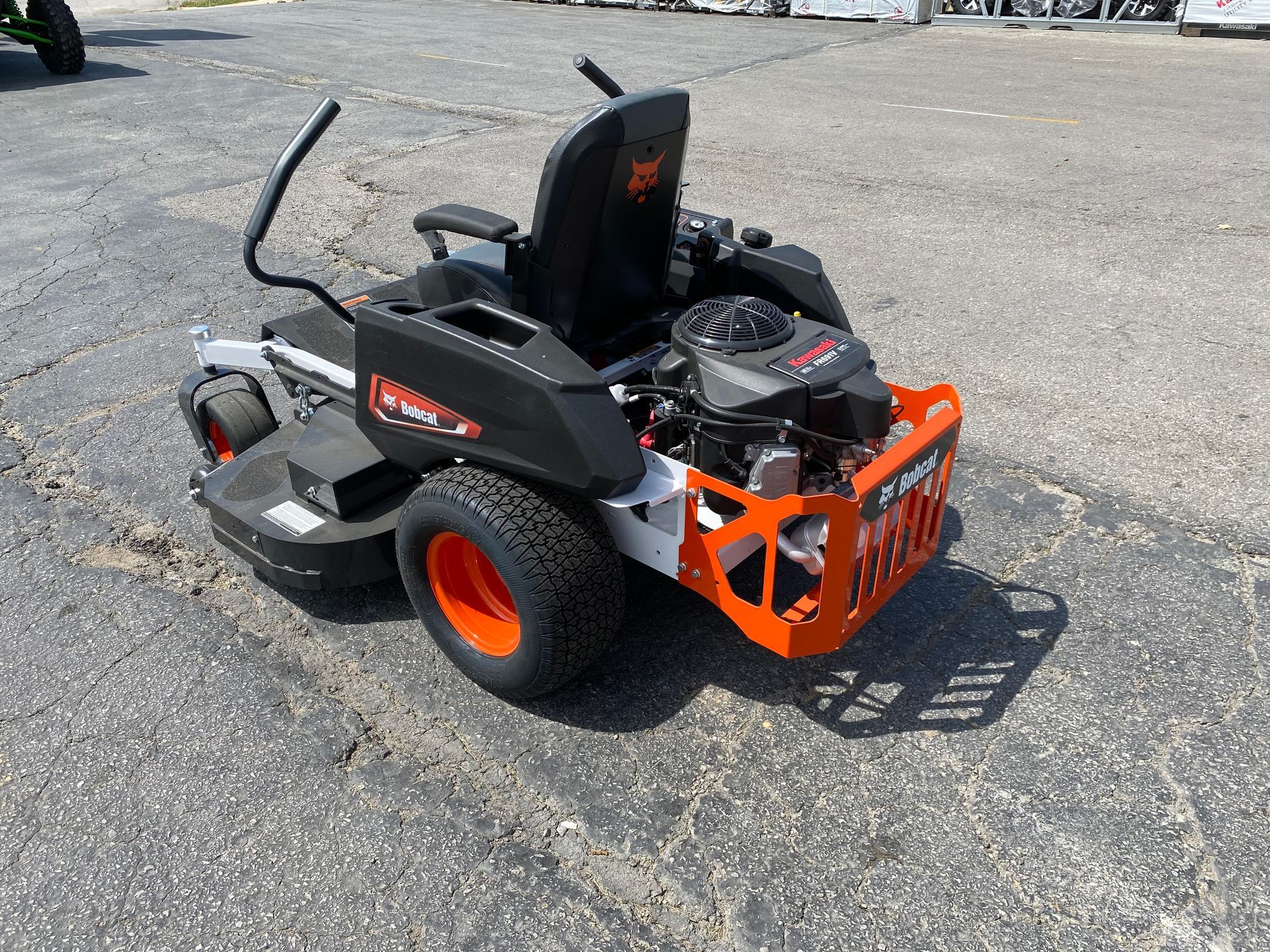 Black and orange Bobcat zero-turn mower on asphalt, sunny outdoor setting.