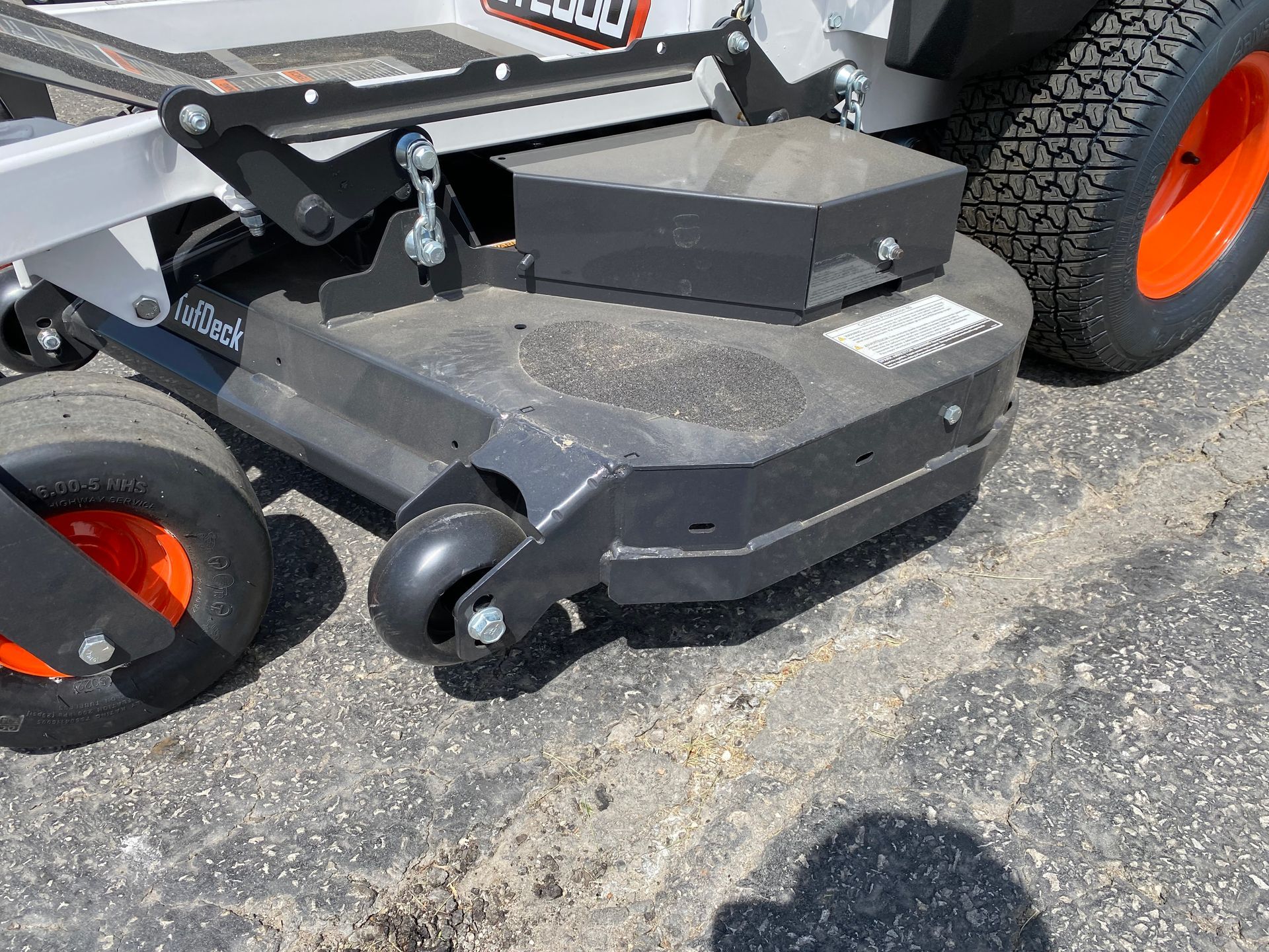 Gray and black lawnmower deck with orange wheels on pavement.
