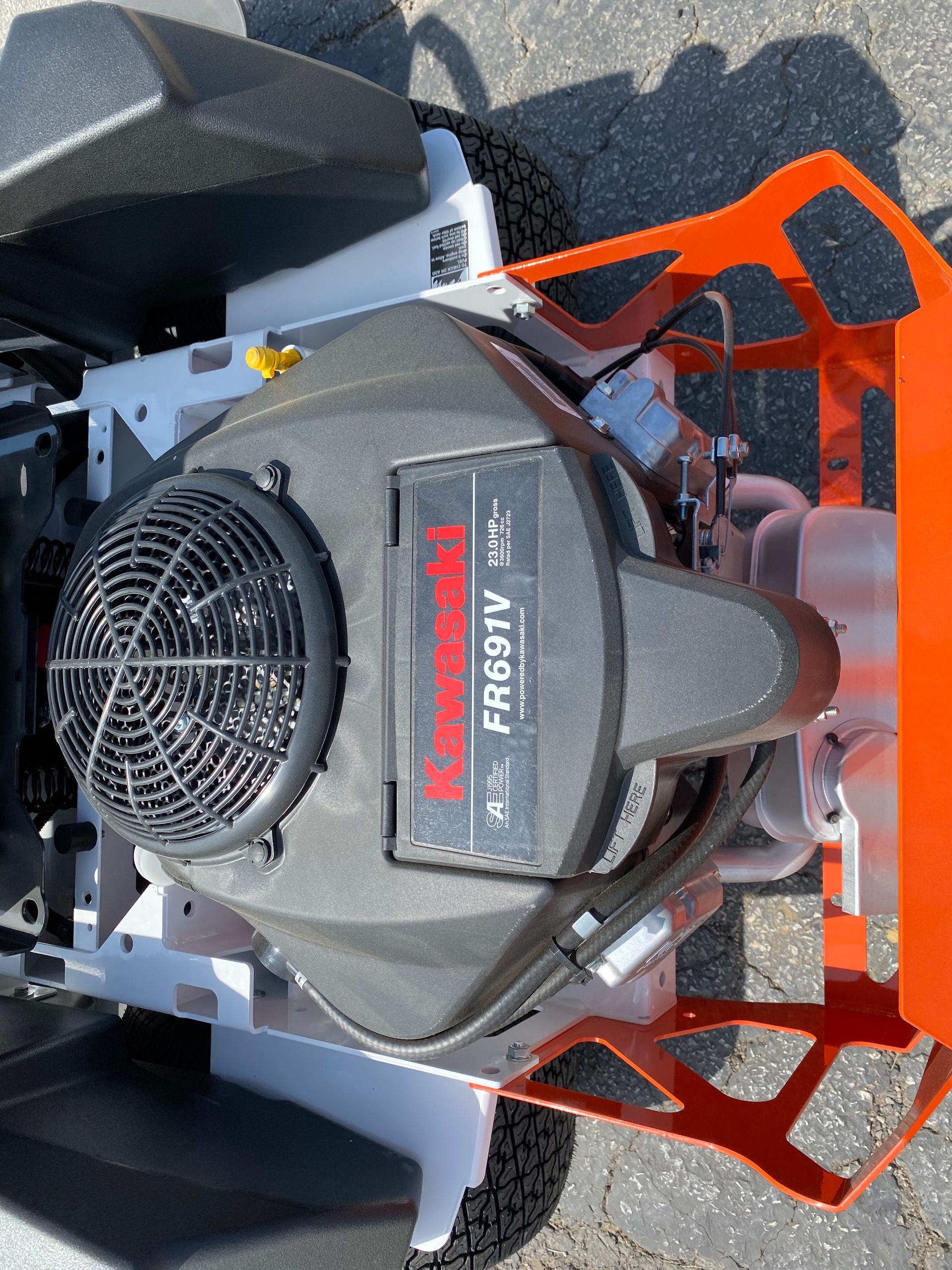 Top view of a zero-turn lawnmower with a Kawasaki engine, orange safety guard, on a paved surface.