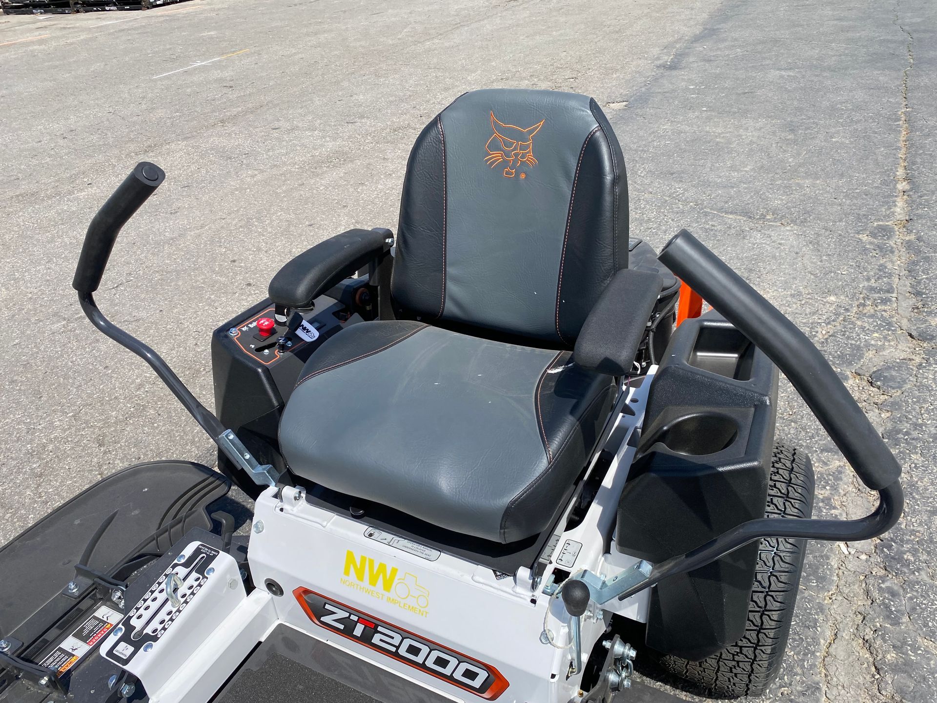 Zero-turn lawn mower. Black and gray seat with armrests. Control levers and cup holder.