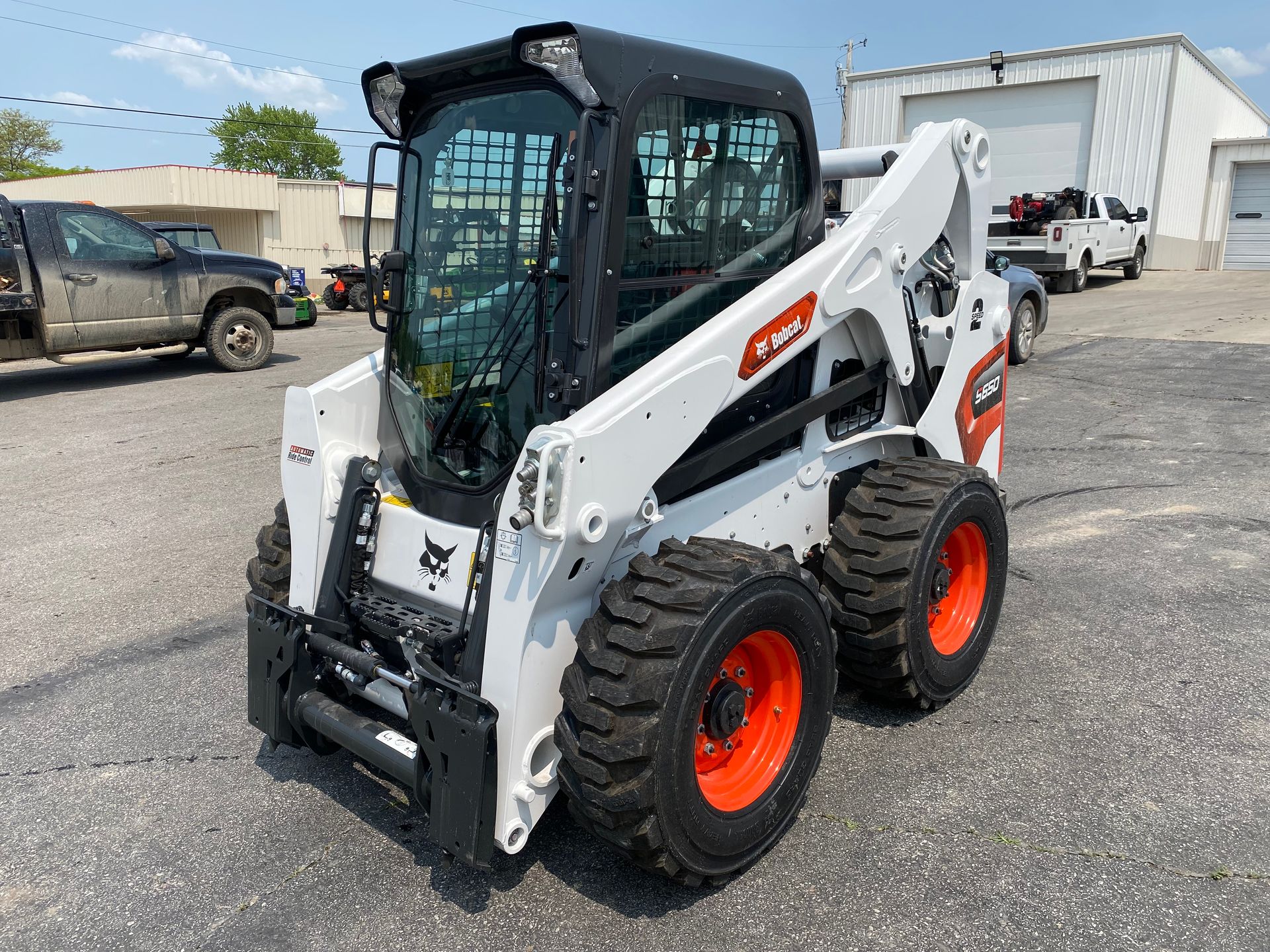 White Bobcat skid-steer loader with black cab, parked outside on a sunny day.