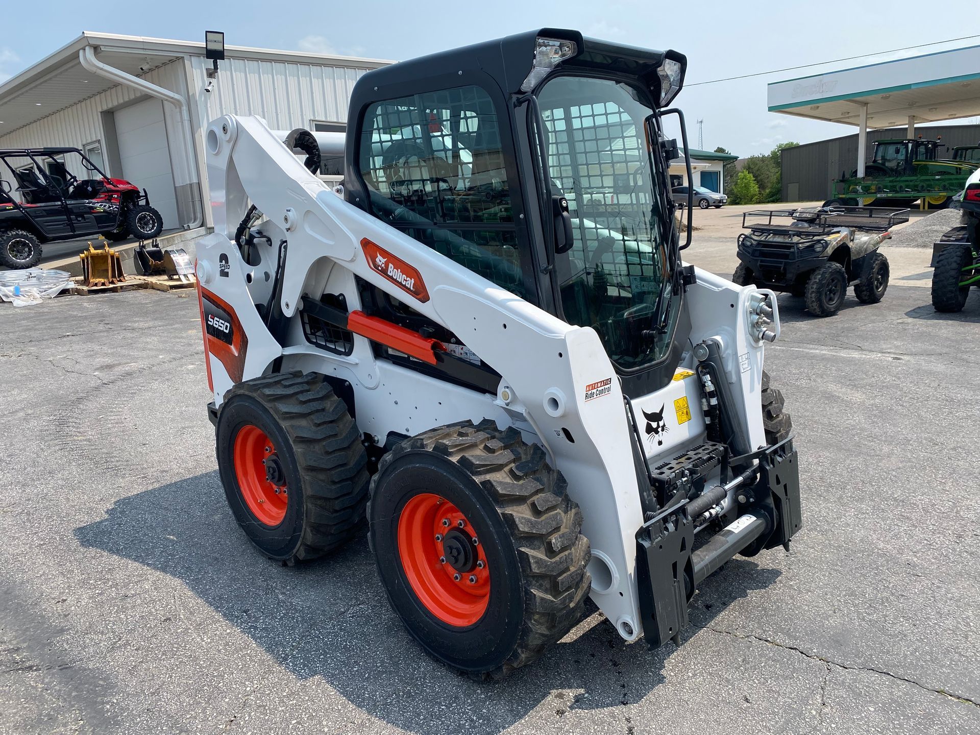 White Bobcat skid-steer loader with black cab, orange wheels, parked outdoors on asphalt.
