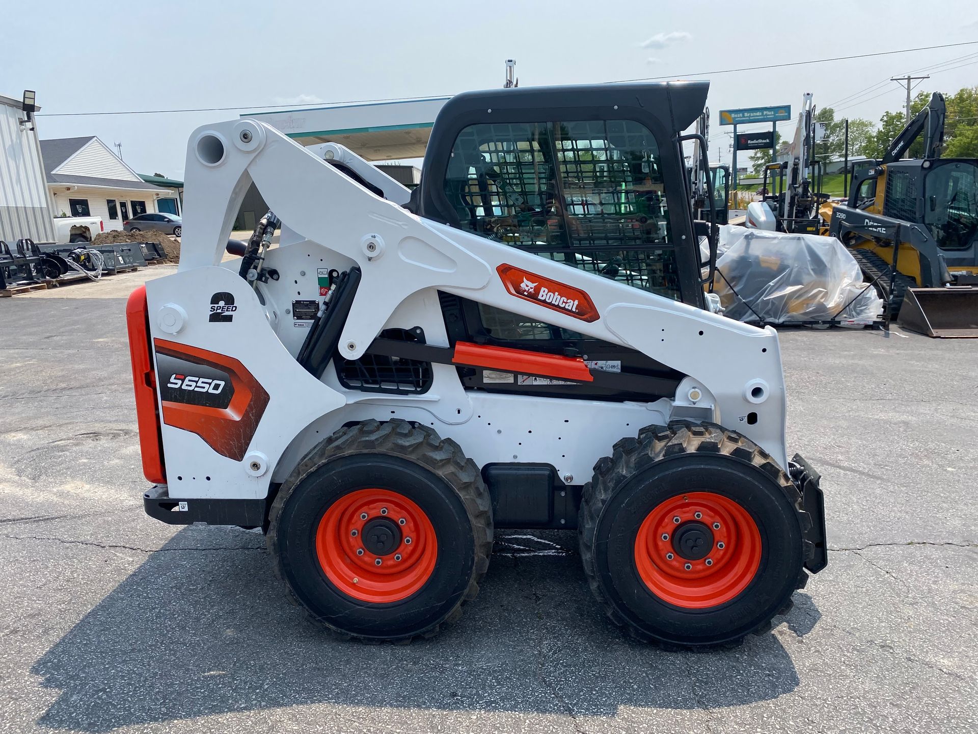 White Bobcat skid-steer loader with orange wheels, parked outdoors on pavement.