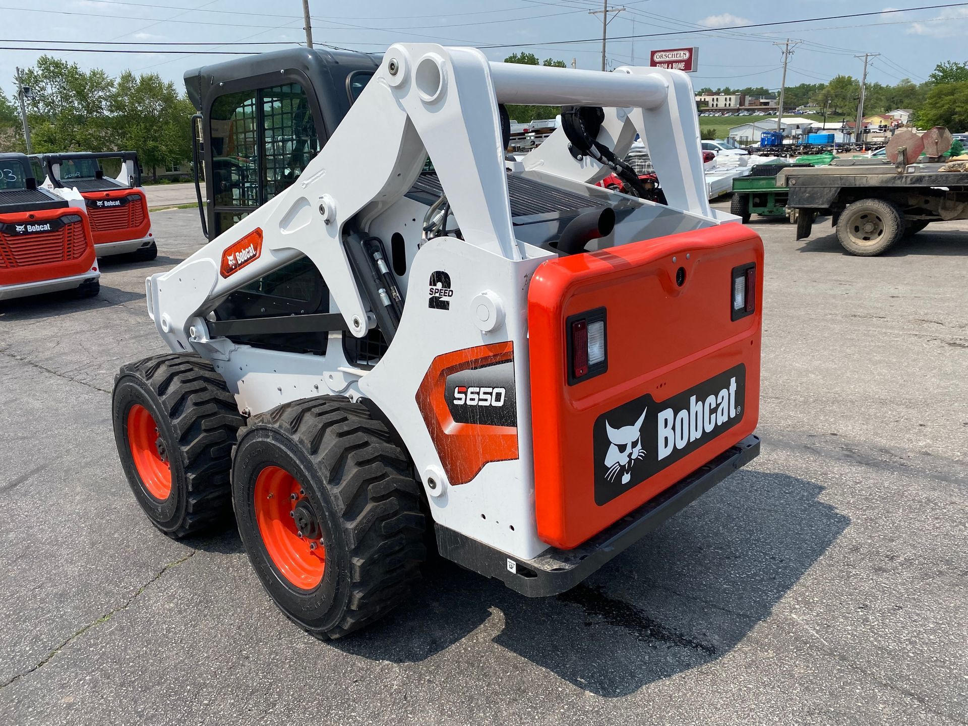 White and orange Bobcat skid-steer loader parked on pavement, with a rear view showing the Bobcat logo.