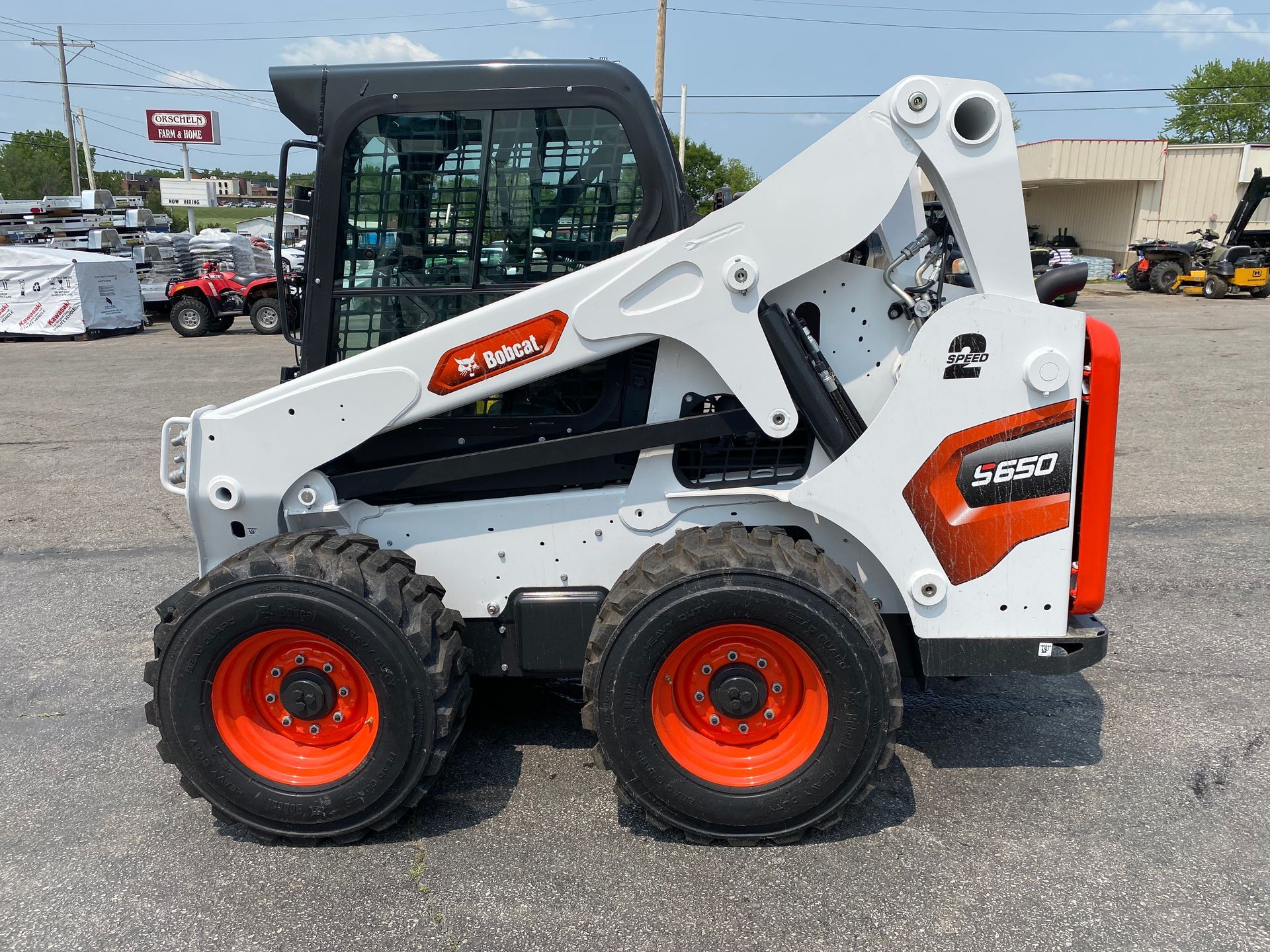 White and orange Bobcat skid-steer loader parked outdoors on asphalt.